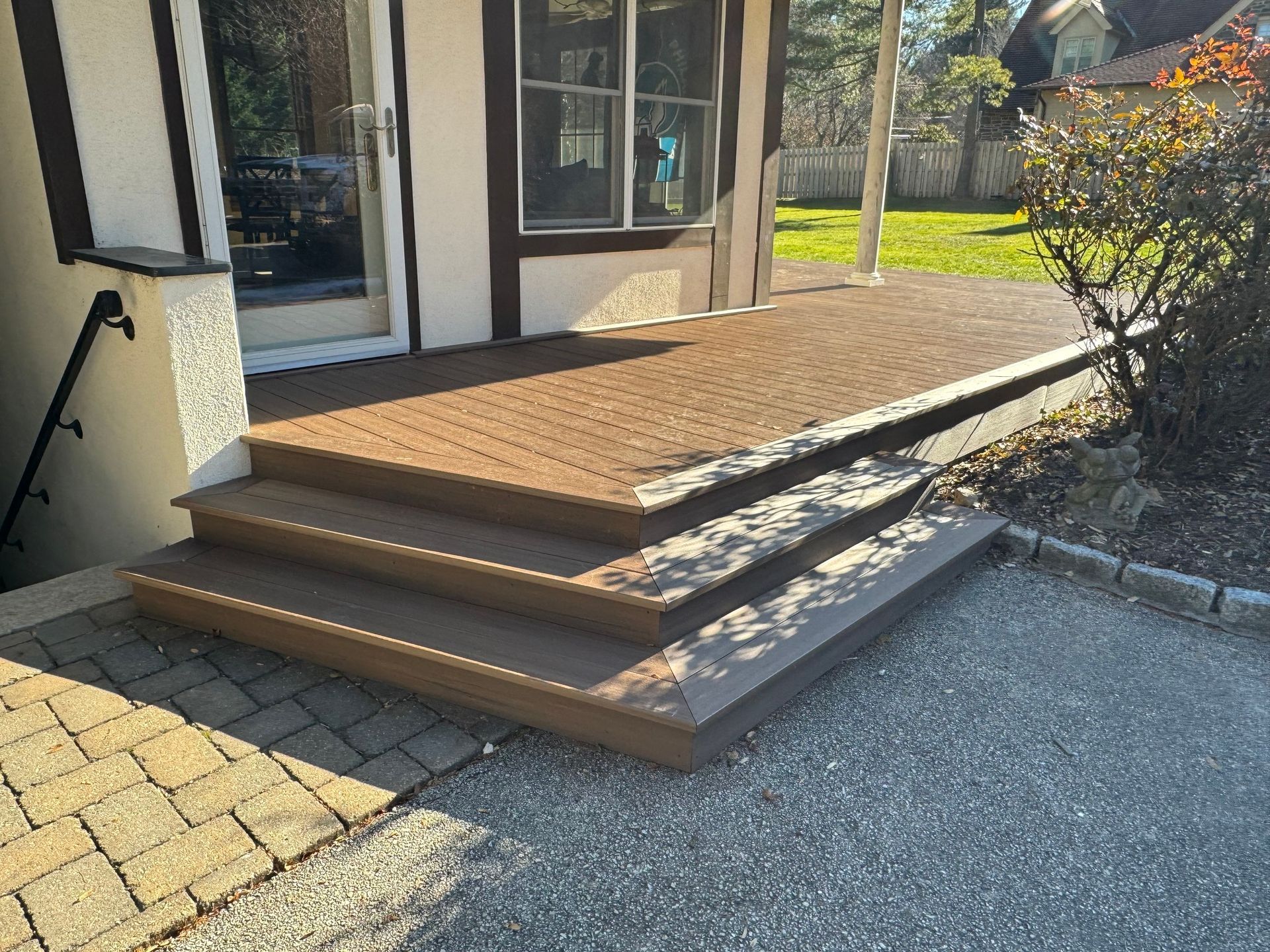 Brown composite deck and steps leading up to a house entrance. Gravel and brick ground.