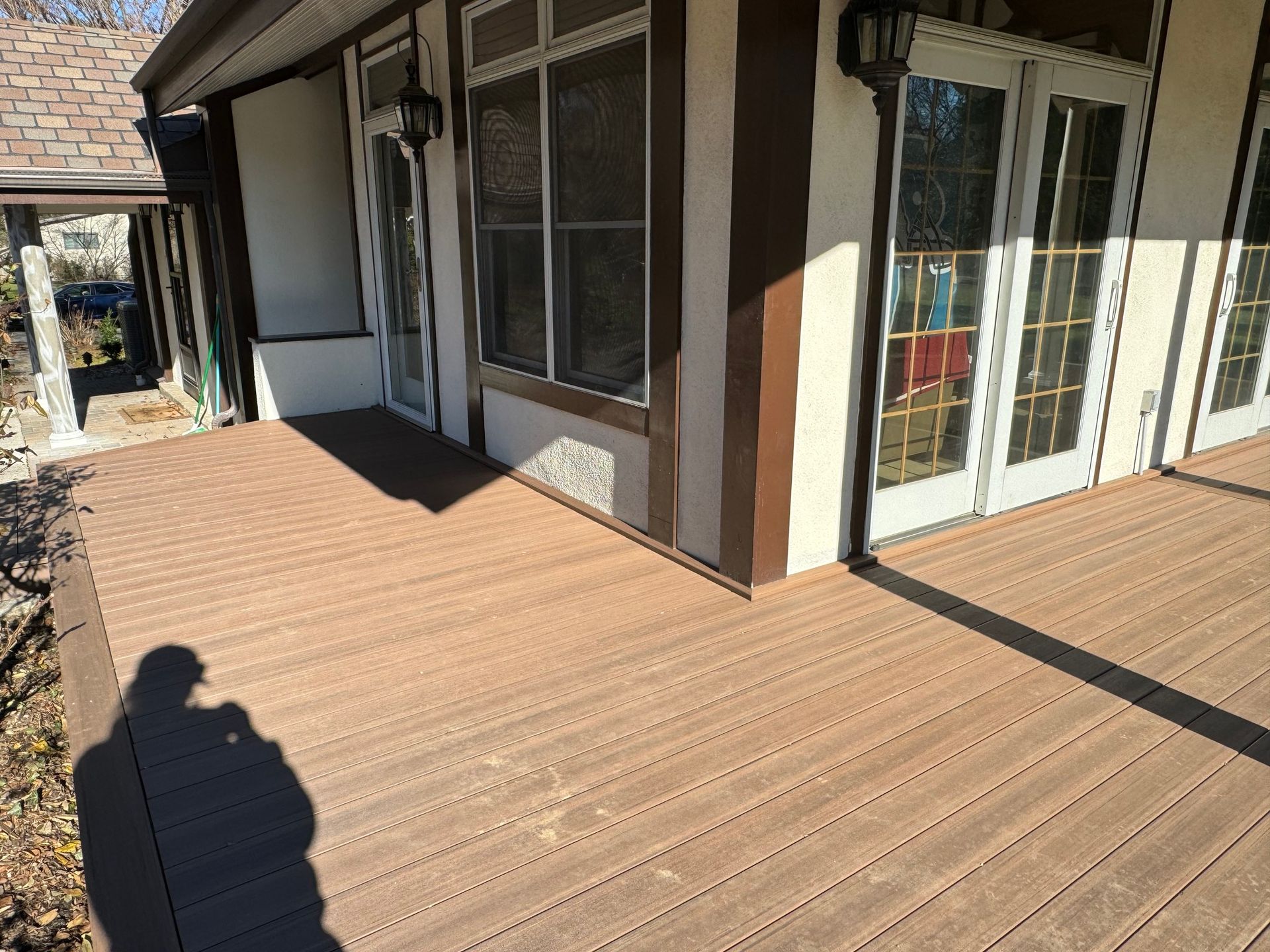 Brown composite deck in front of a house with white walls, brown trim, and glass doors/windows.