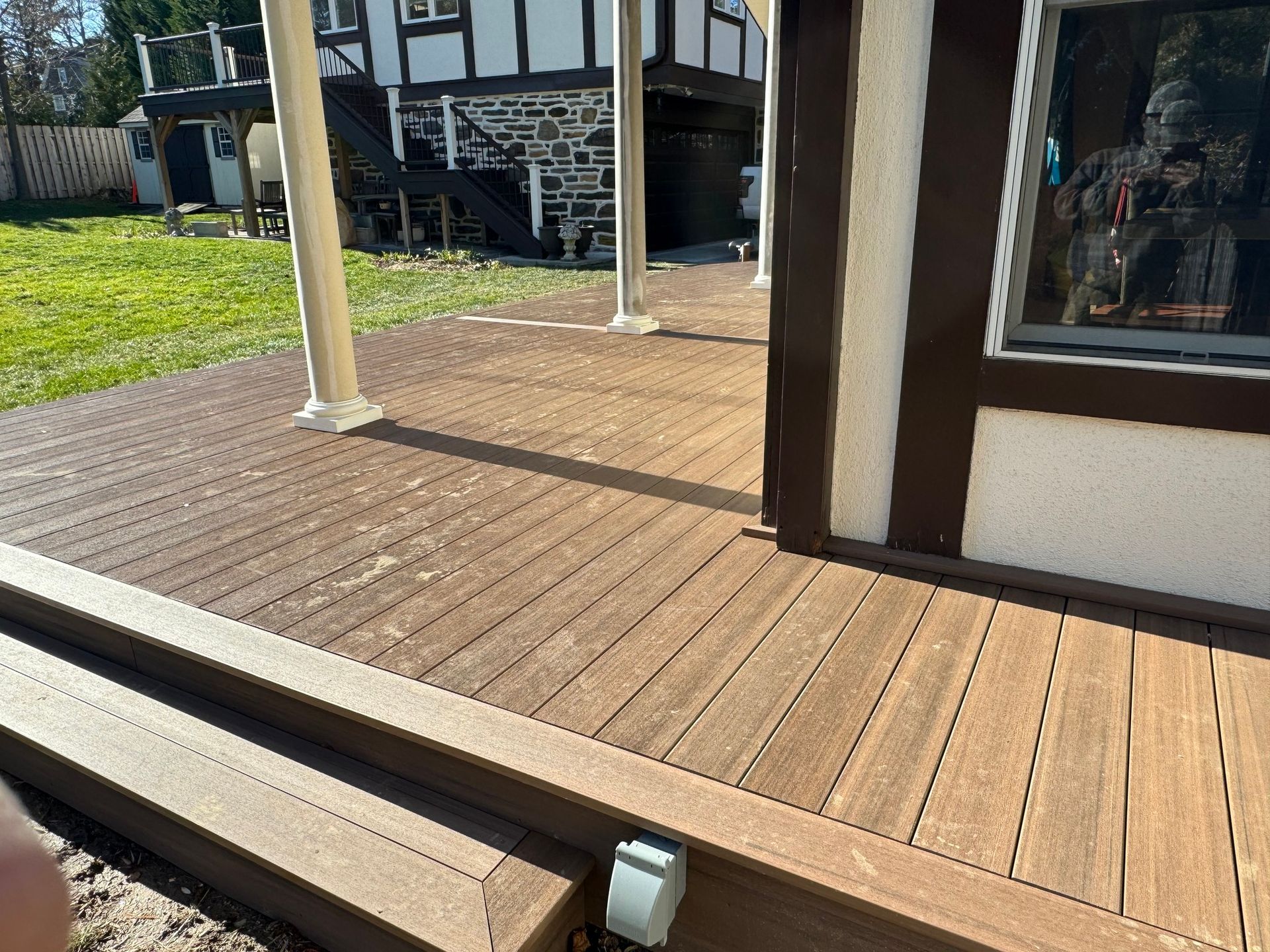 Wooden deck with brown and white house and pillars in the background. Sunny day.