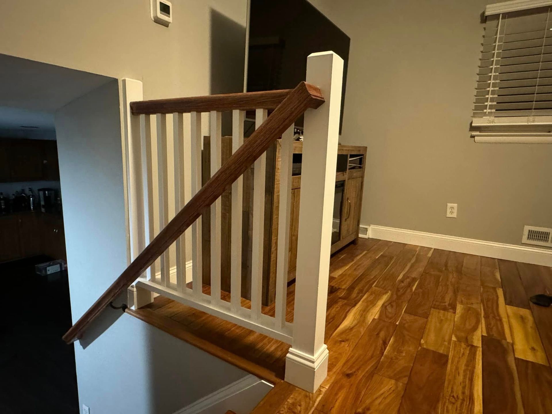 Wooden handrail and white balusters on a staircase with hardwood flooring.