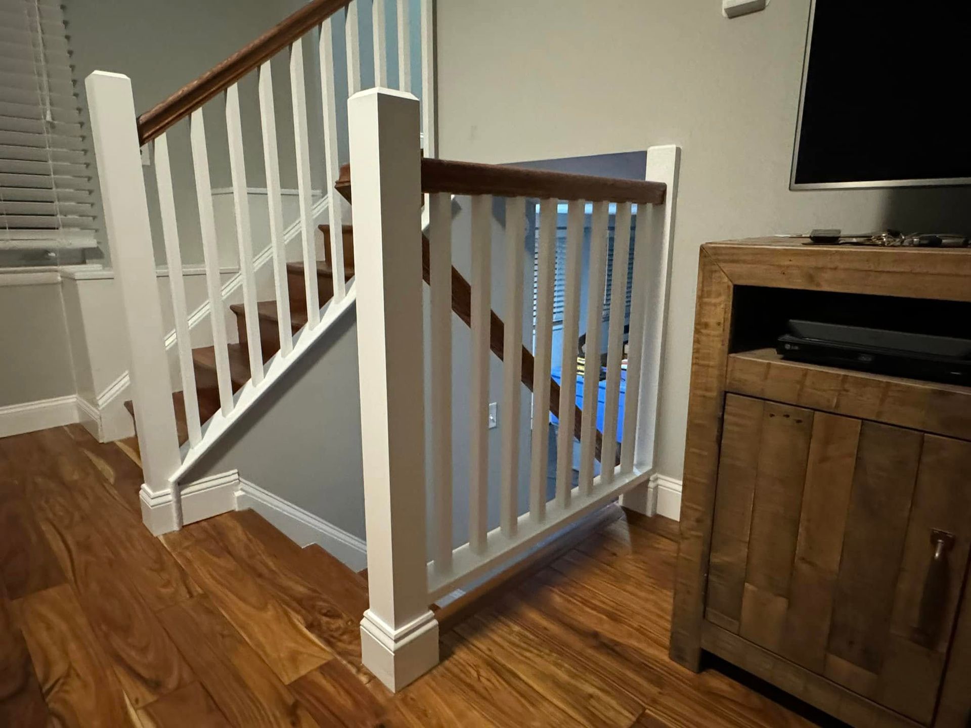 Wooden staircase with white railings and a safety gate near a wooden cabinet.