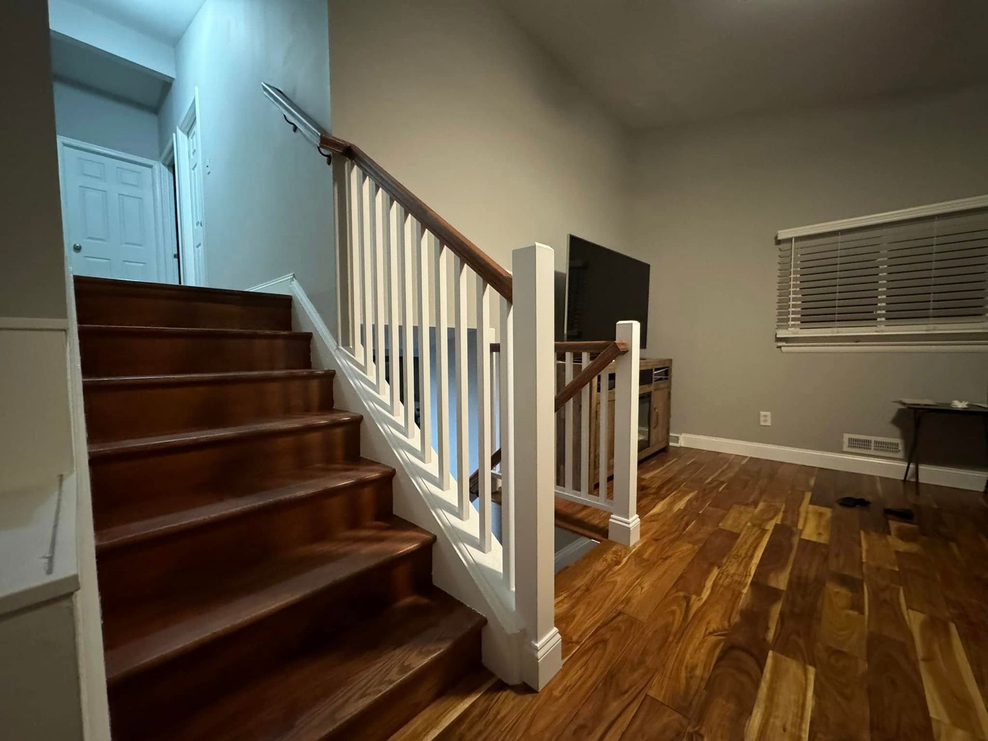Wooden staircase with white banister, leading up to a doorway. Hardwood floors and a TV on a stand in a room.