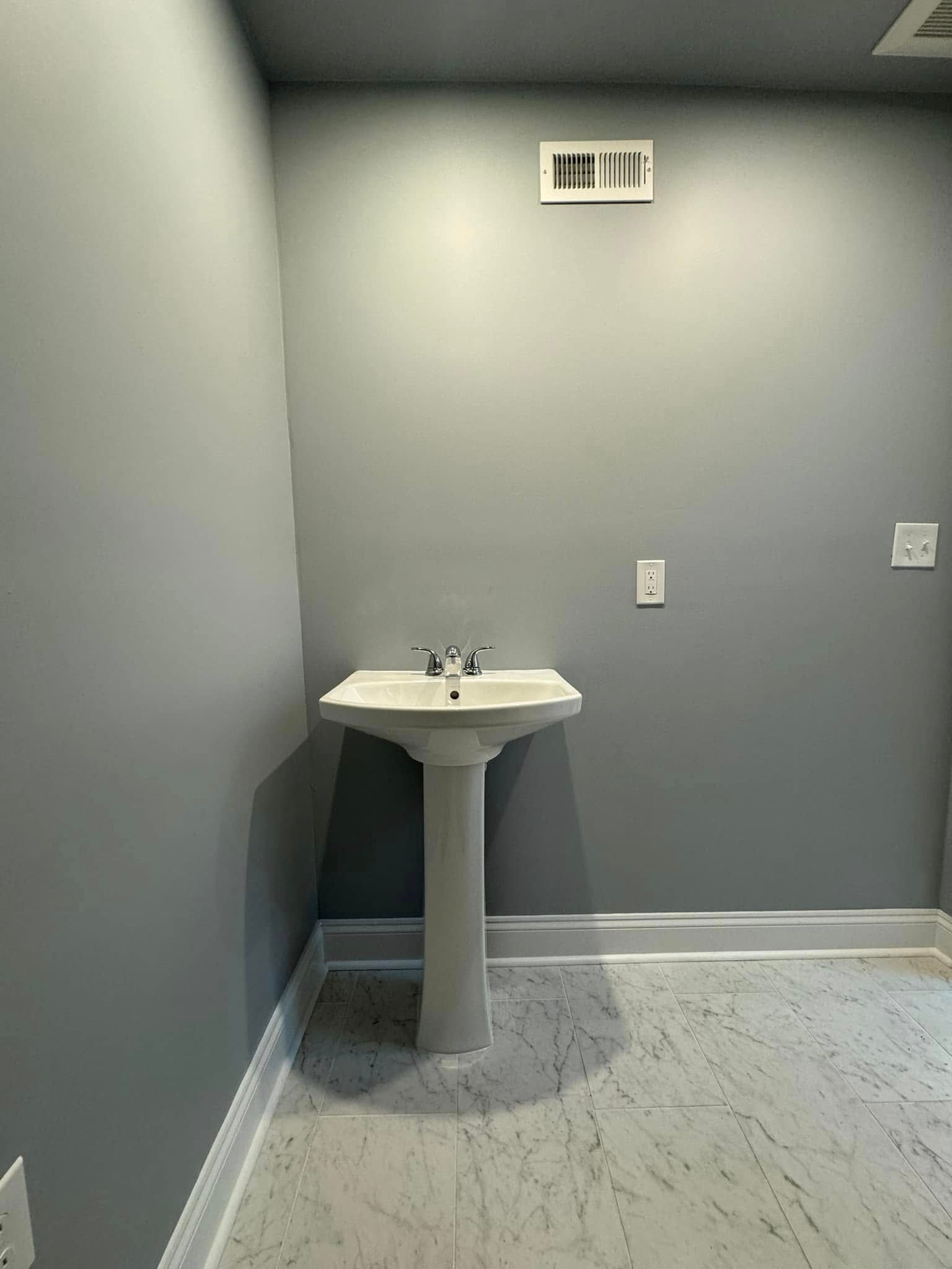 Pedestal sink in a small room with grey walls and a patterned floor.