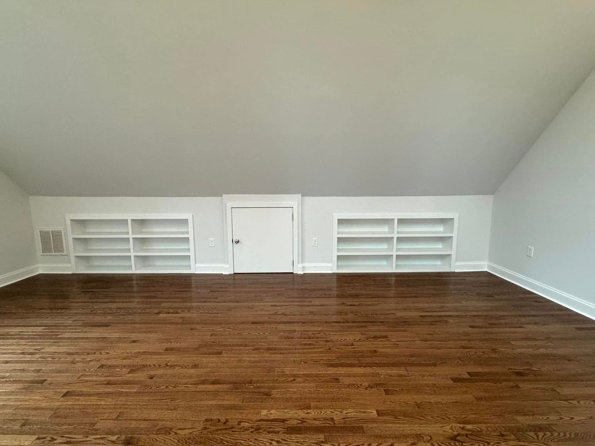 Empty room with hardwood floors, white walls, built-in bookshelves, and a door centered.