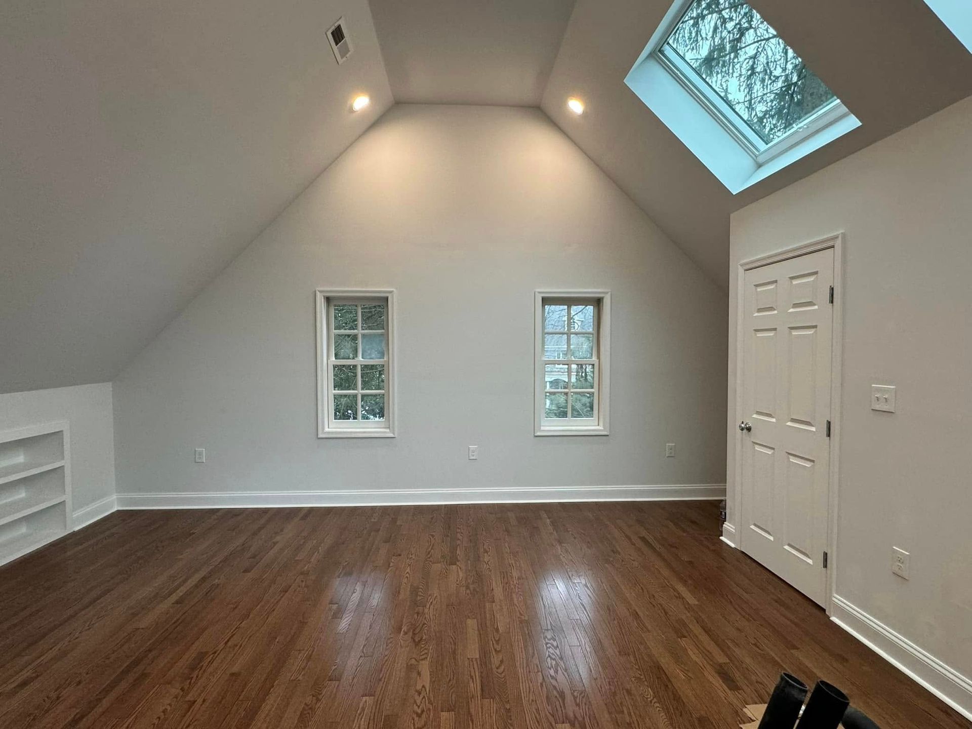 Spacious room with sloped ceiling, skylight, two windows, and dark hardwood floors.