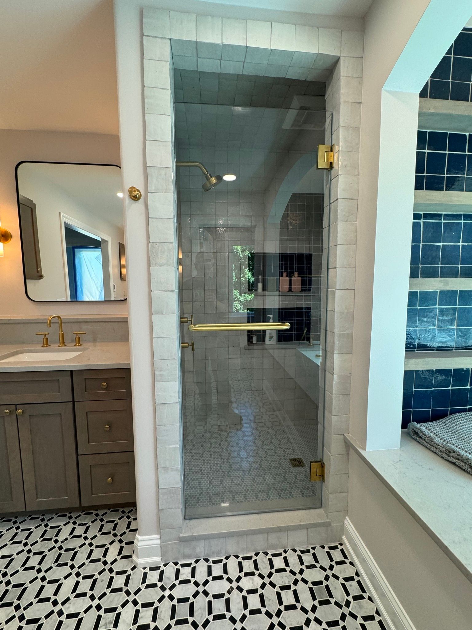 Bathroom with a clear glass shower door, gold fixtures, and patterned black and white tile.