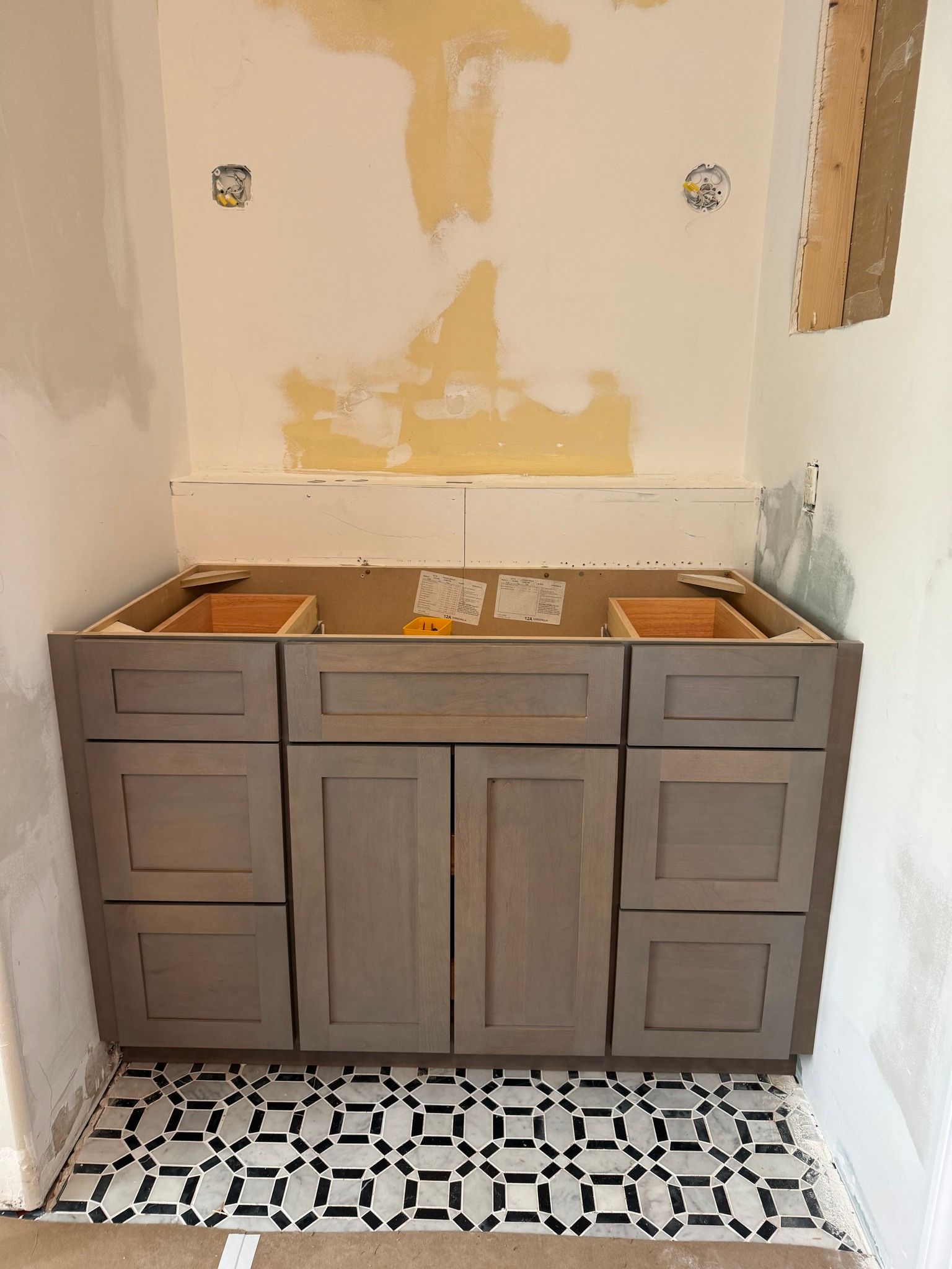 Bathroom vanity installed on patterned tile floor, unfinished wall above.