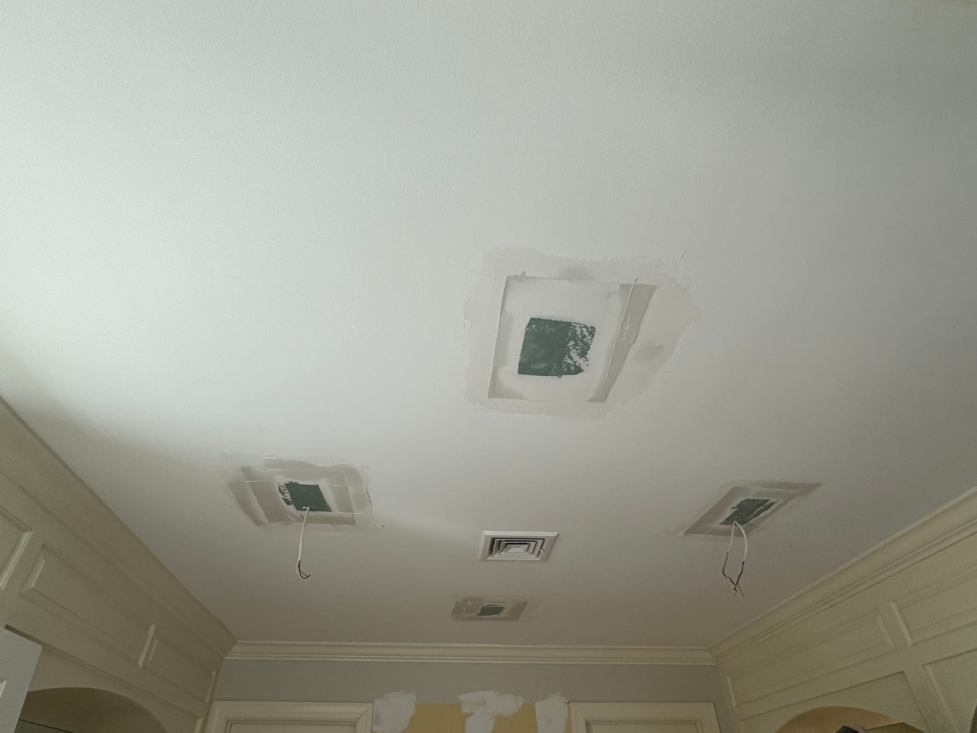 White ceiling with drywall patches around recessed light openings. Wires hang from some openings.