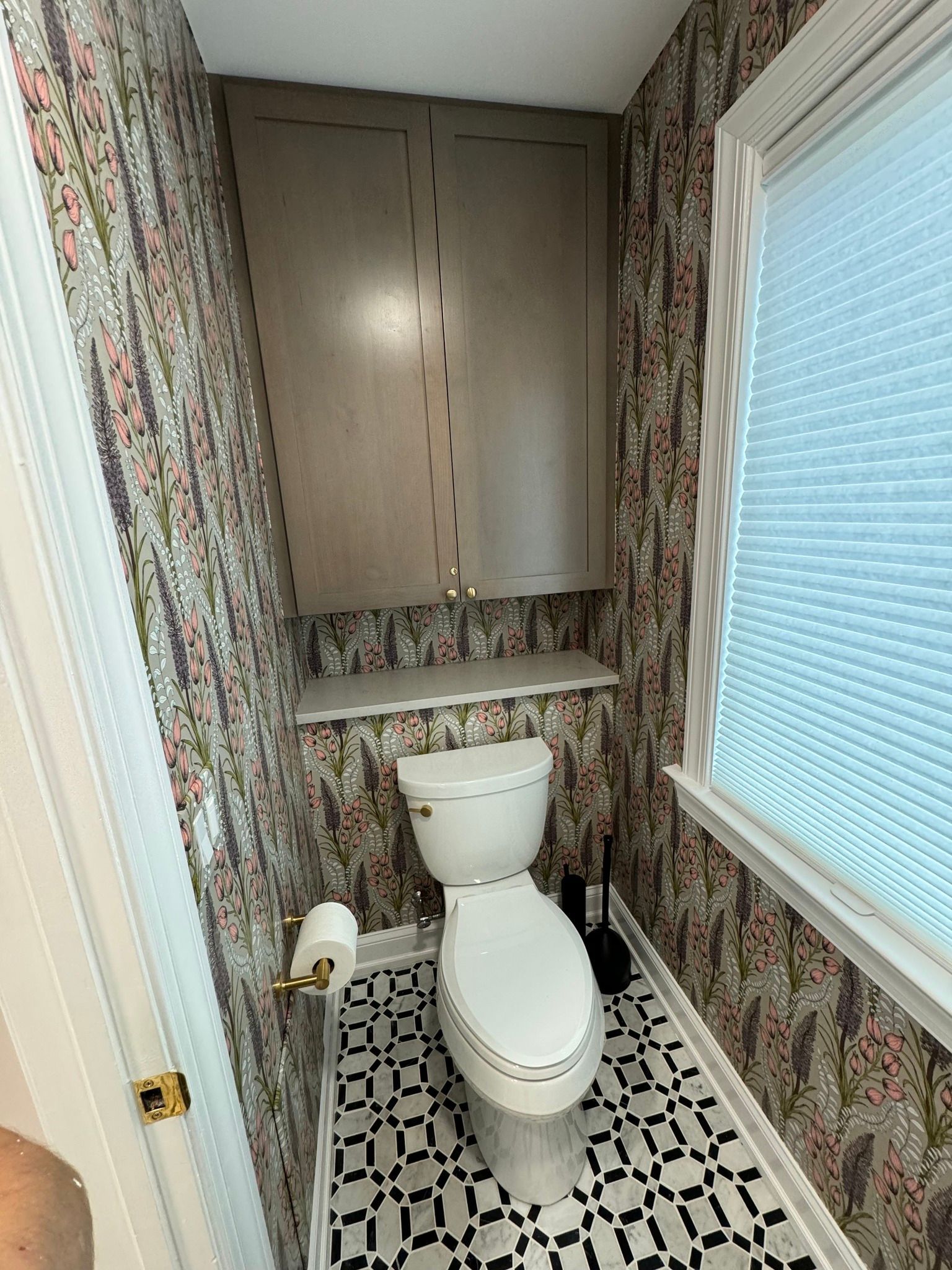 Small bathroom with floral wallpaper, a toilet, cabinet, and patterned floor.