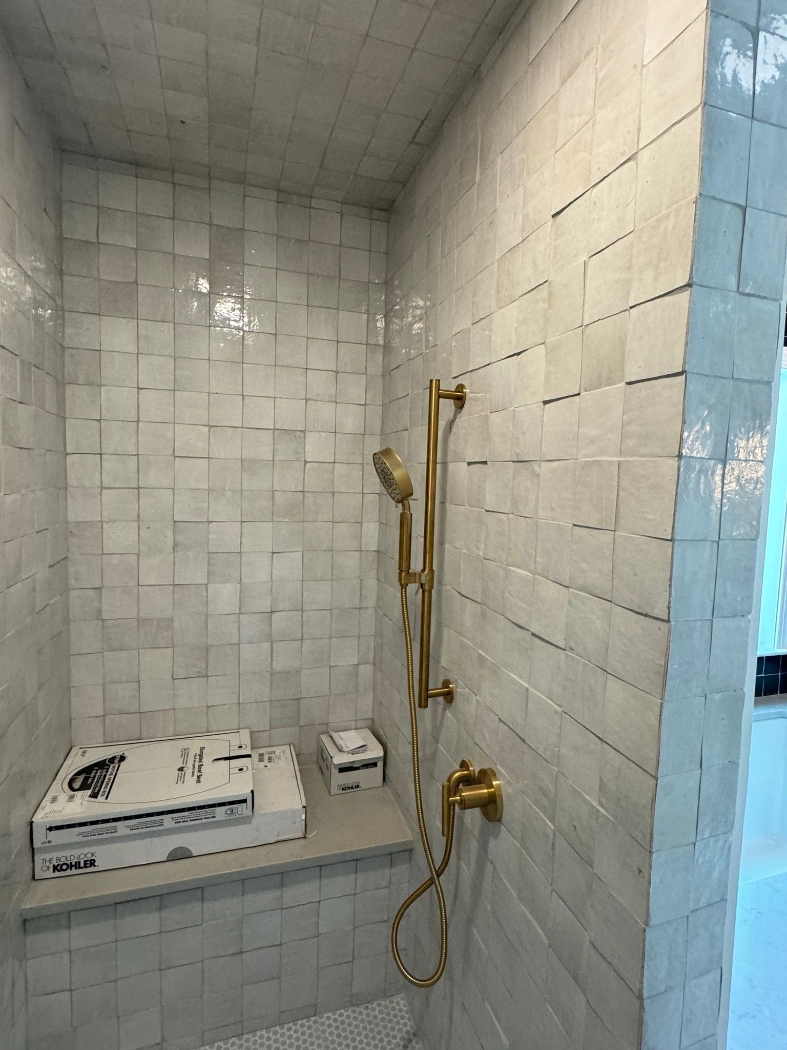 Tiled shower with gold fixtures, a bench, and two boxes.