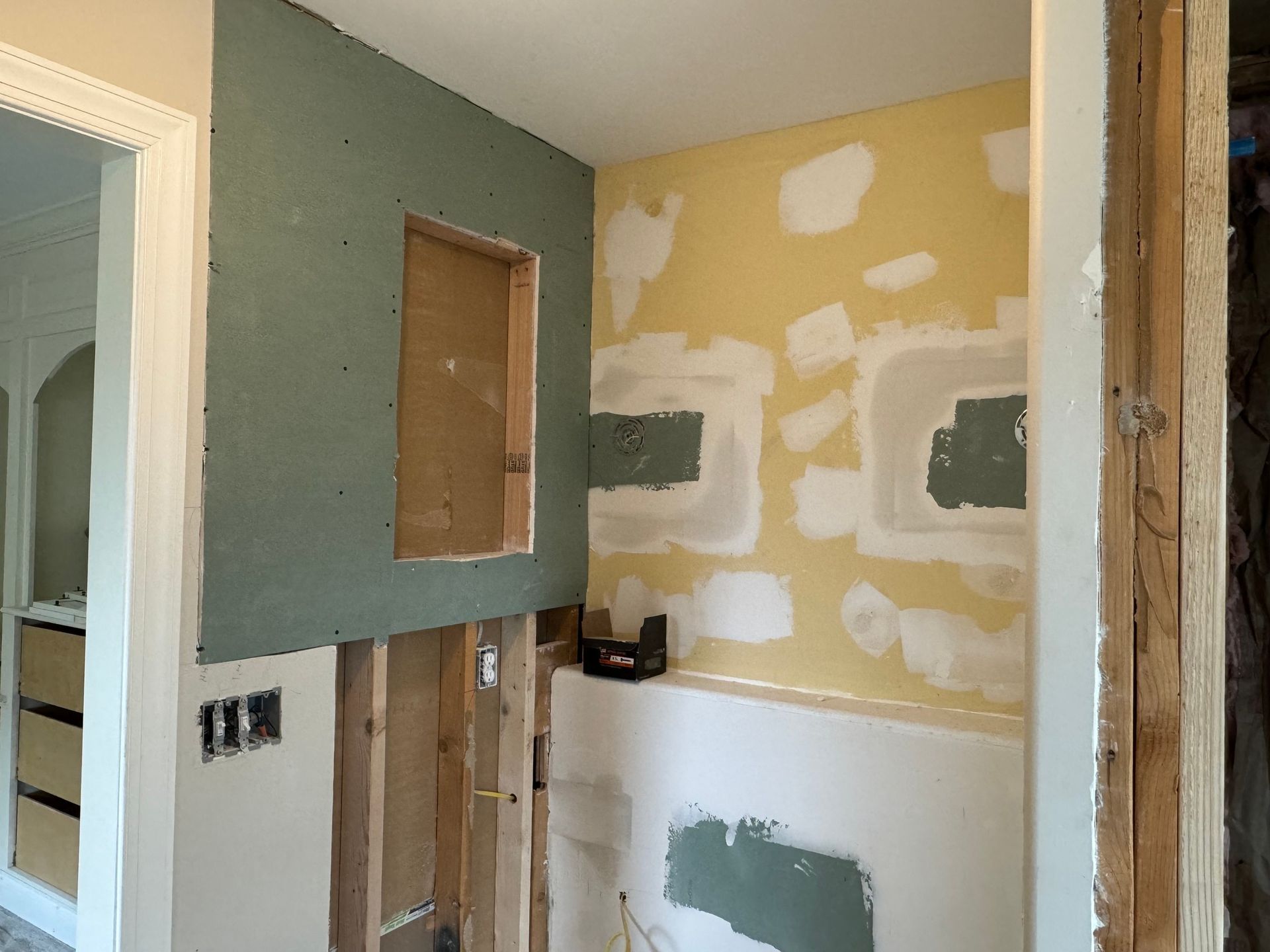 Bathroom under renovation: green drywall, exposed studs, partially plastered walls in yellow and white.