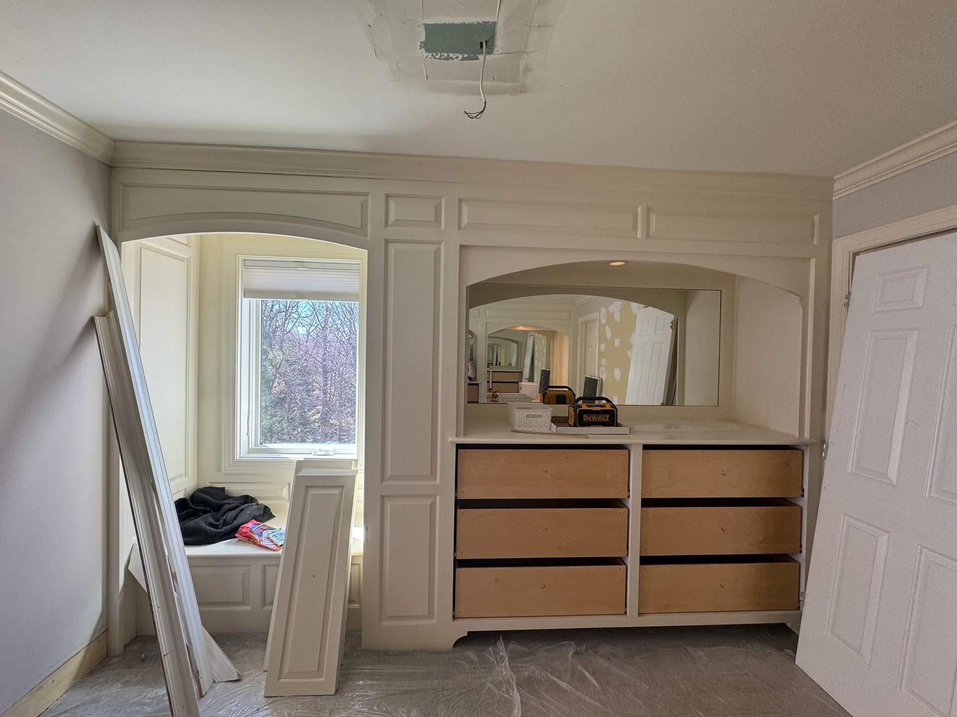 Bedroom built-in cabinet with drawers, a window seat, and a mirror, under construction with unfinished trim.