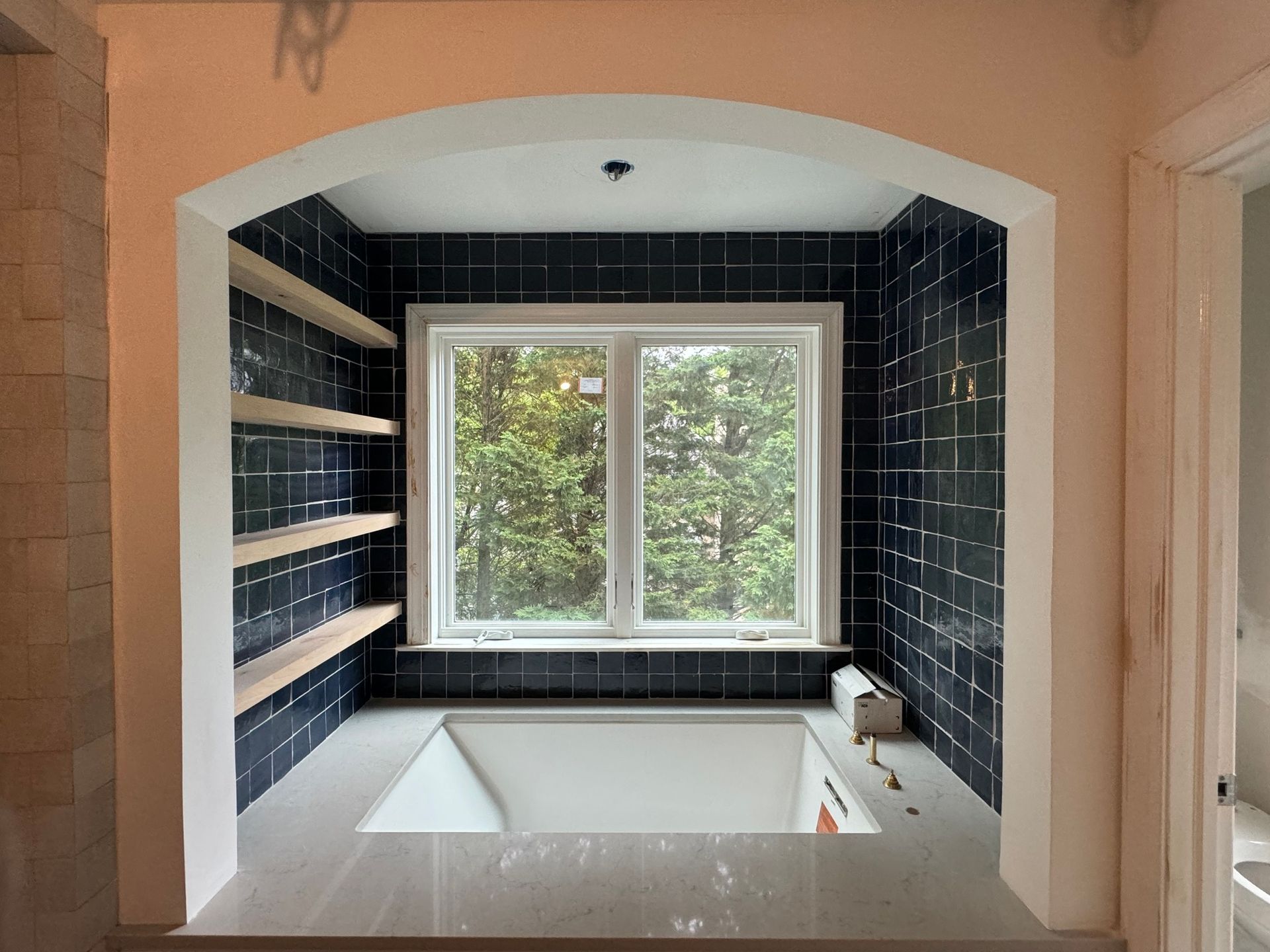 Bathroom alcove with tiled walls, window, built-in shelves, and a tub.