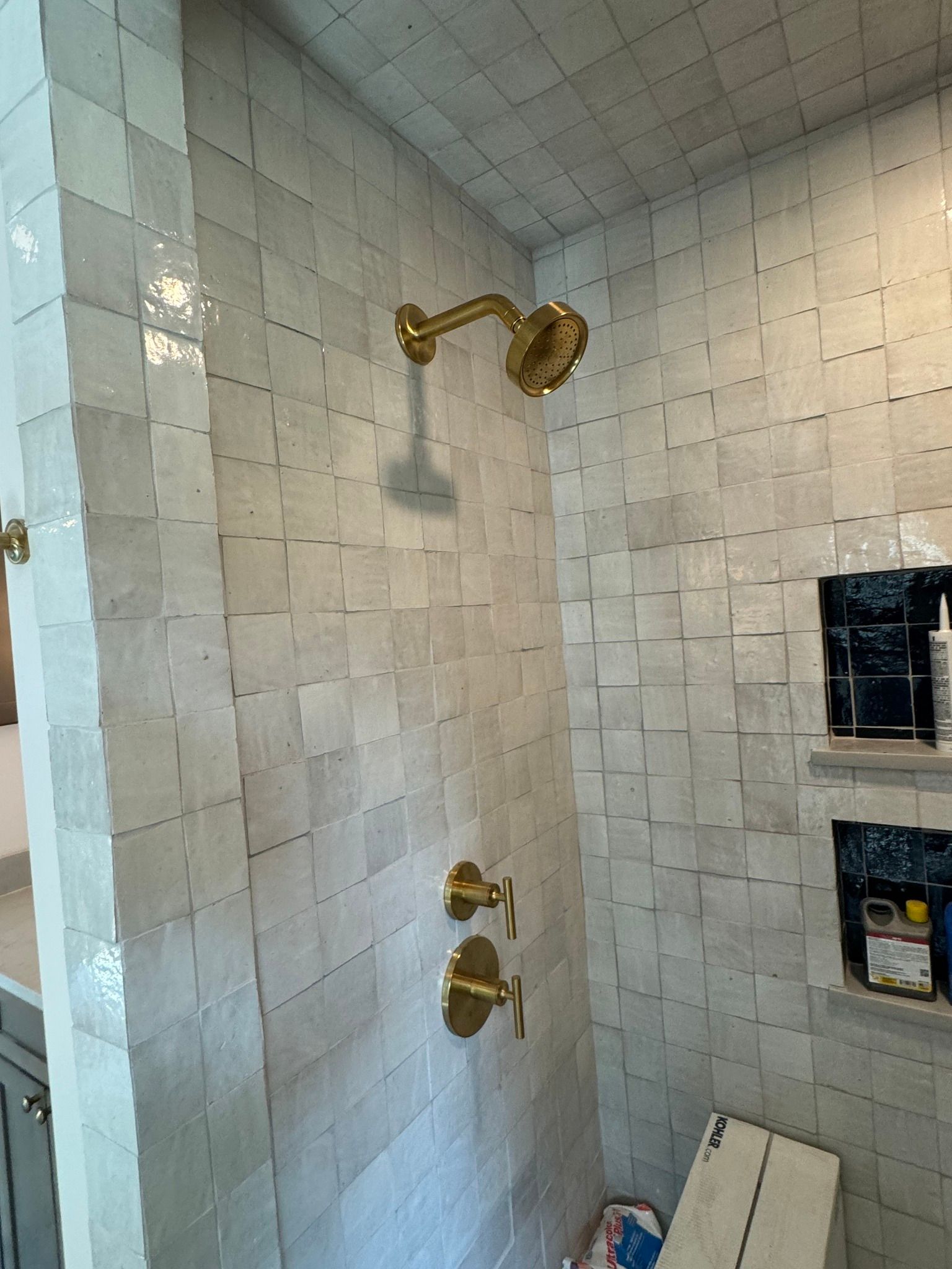 Gold shower fixtures on white square tile walls.
