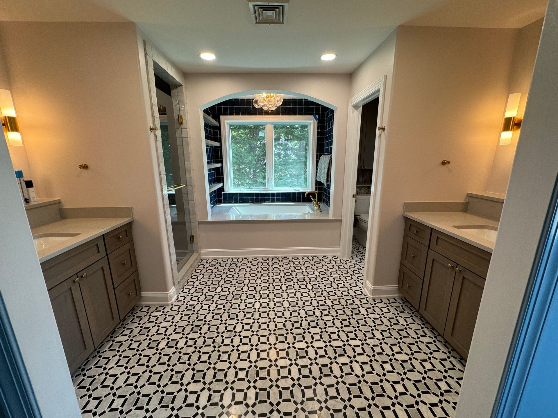 Bathroom with patterned tile floor, two vanities, and a walk-in shower. A large window and a tub are in the background.