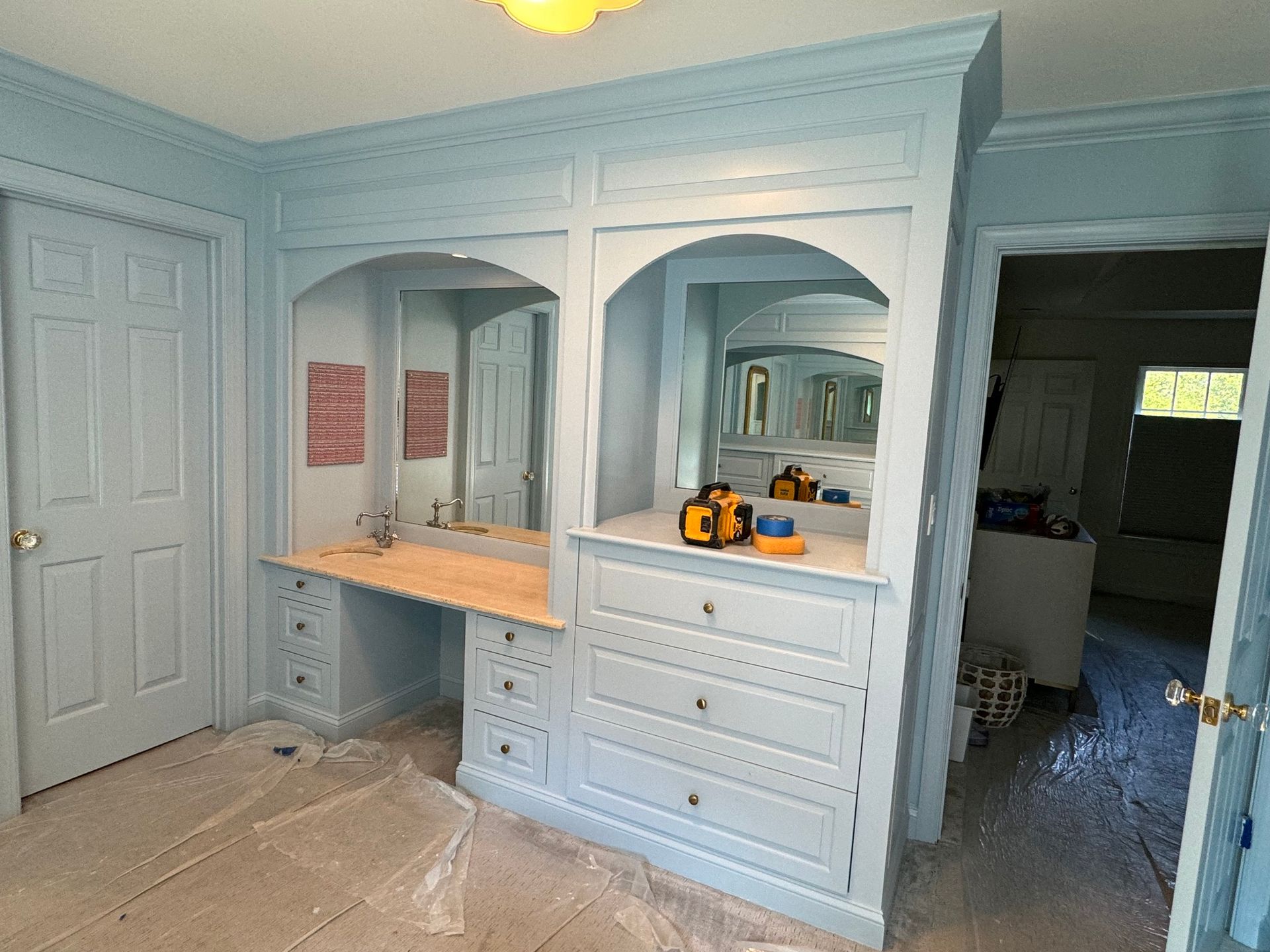 Light blue vanity and built-in drawers with arched mirrors in a bedroom. Door on the left.