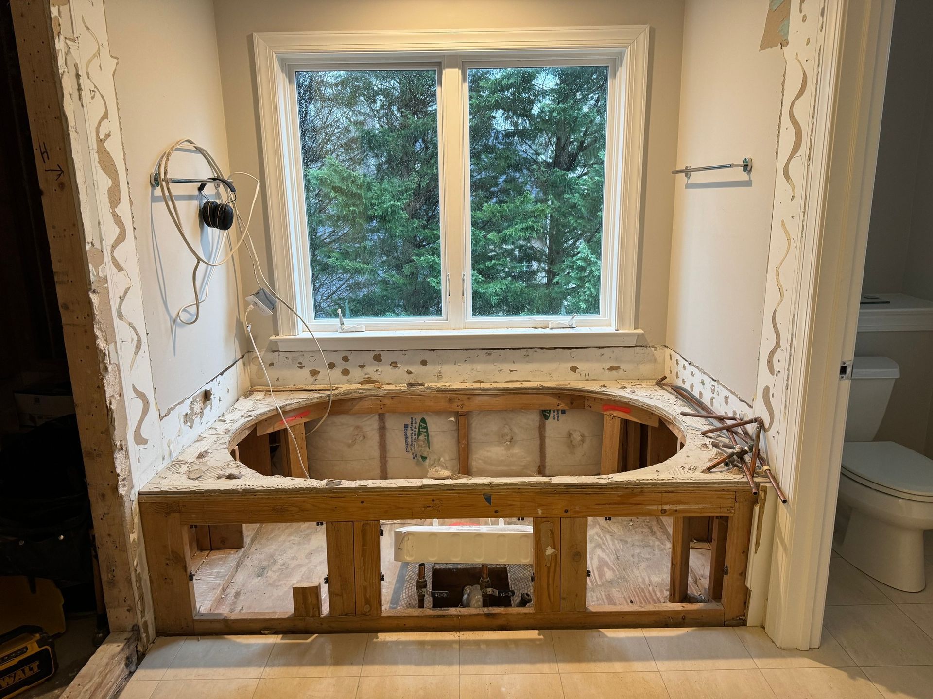 Bathroom remodel with exposed tub frame beneath a window; demolition in progress.