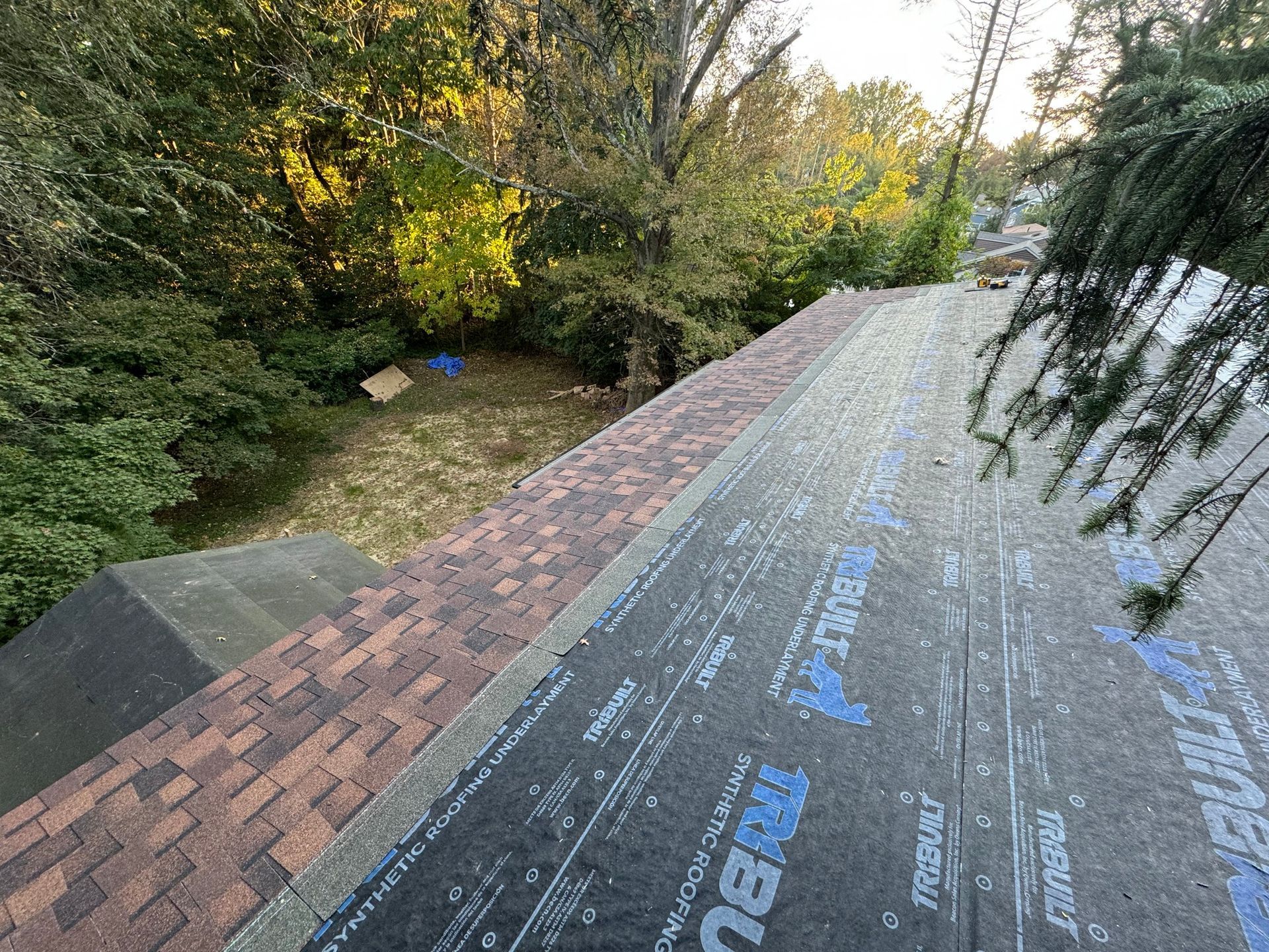 Rooftop view of house with new shingles being installed.  Woodland background and fall colors.