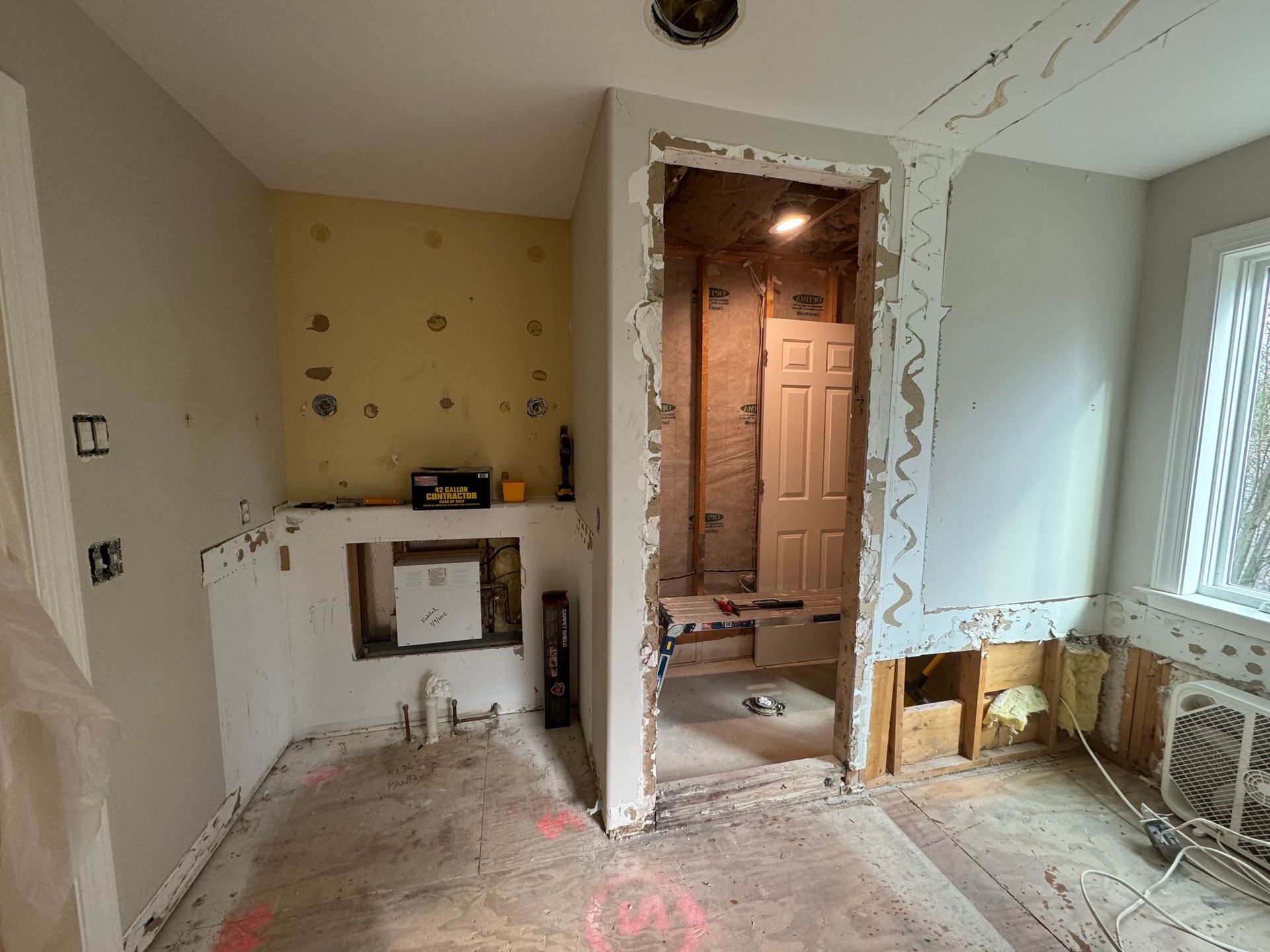 Bathroom undergoing renovation; exposed studs, drywall removal. Gray walls, rough floor, and open doorway.