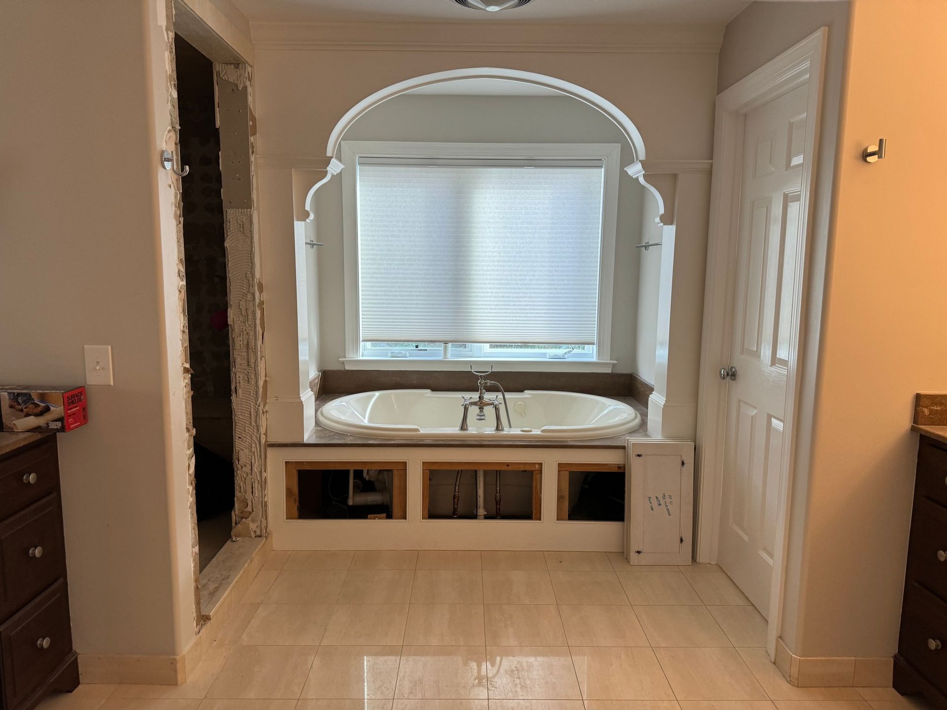 Bathroom with a soaking tub in front of a window, and wood cabinetry.