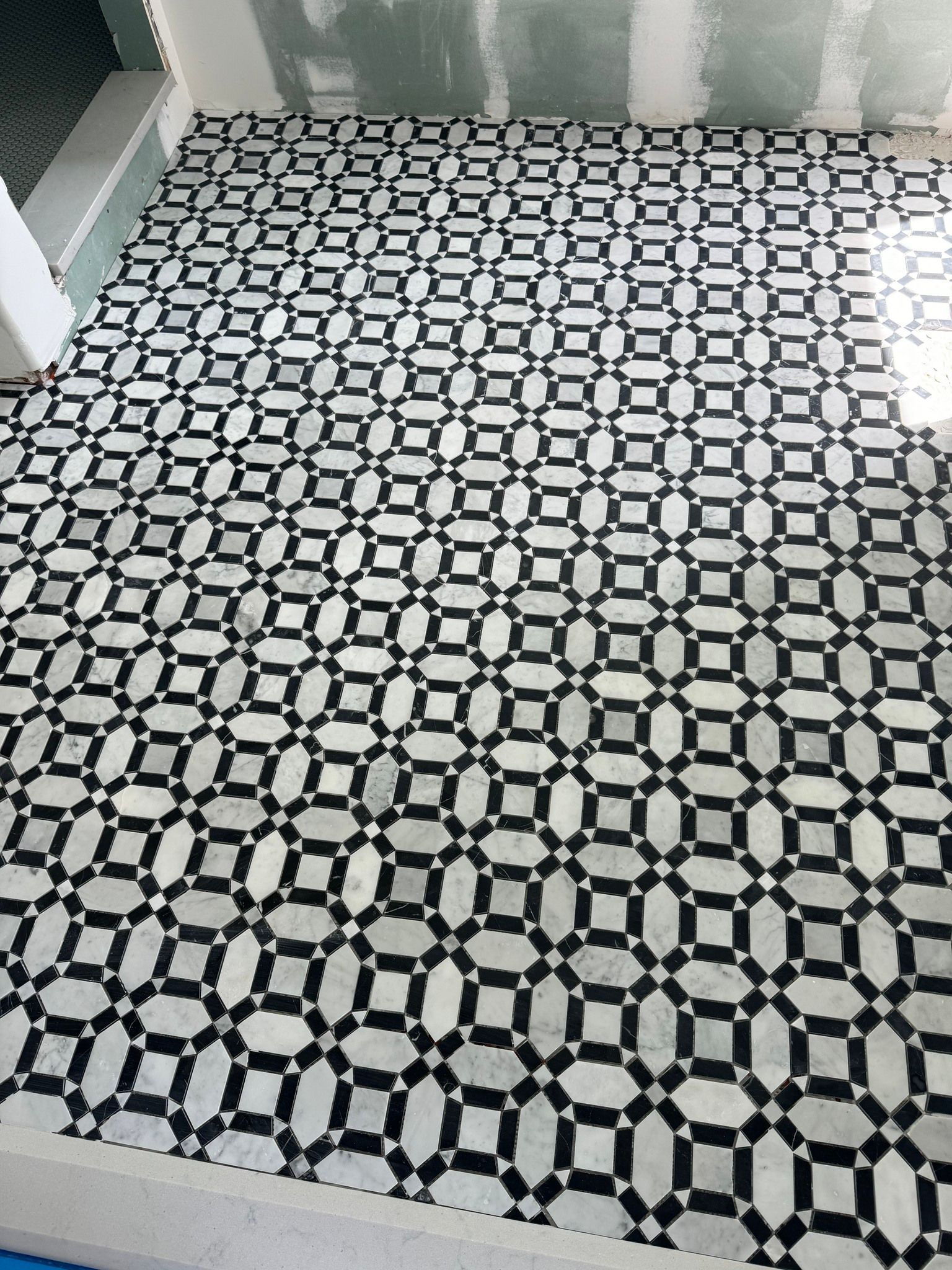 Black and white patterned tile floor in a room under construction, with walls and a ledge visible.