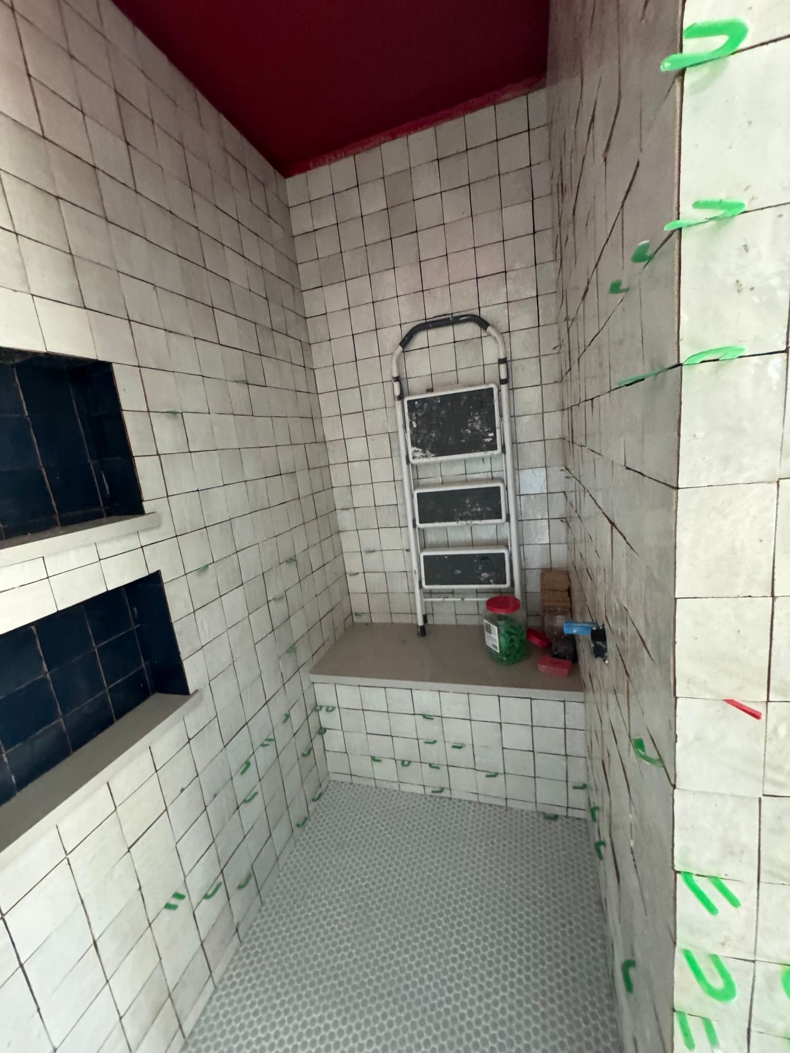 Bathroom under construction, tiled walls and floor, red ceiling, step ladder, green tape.