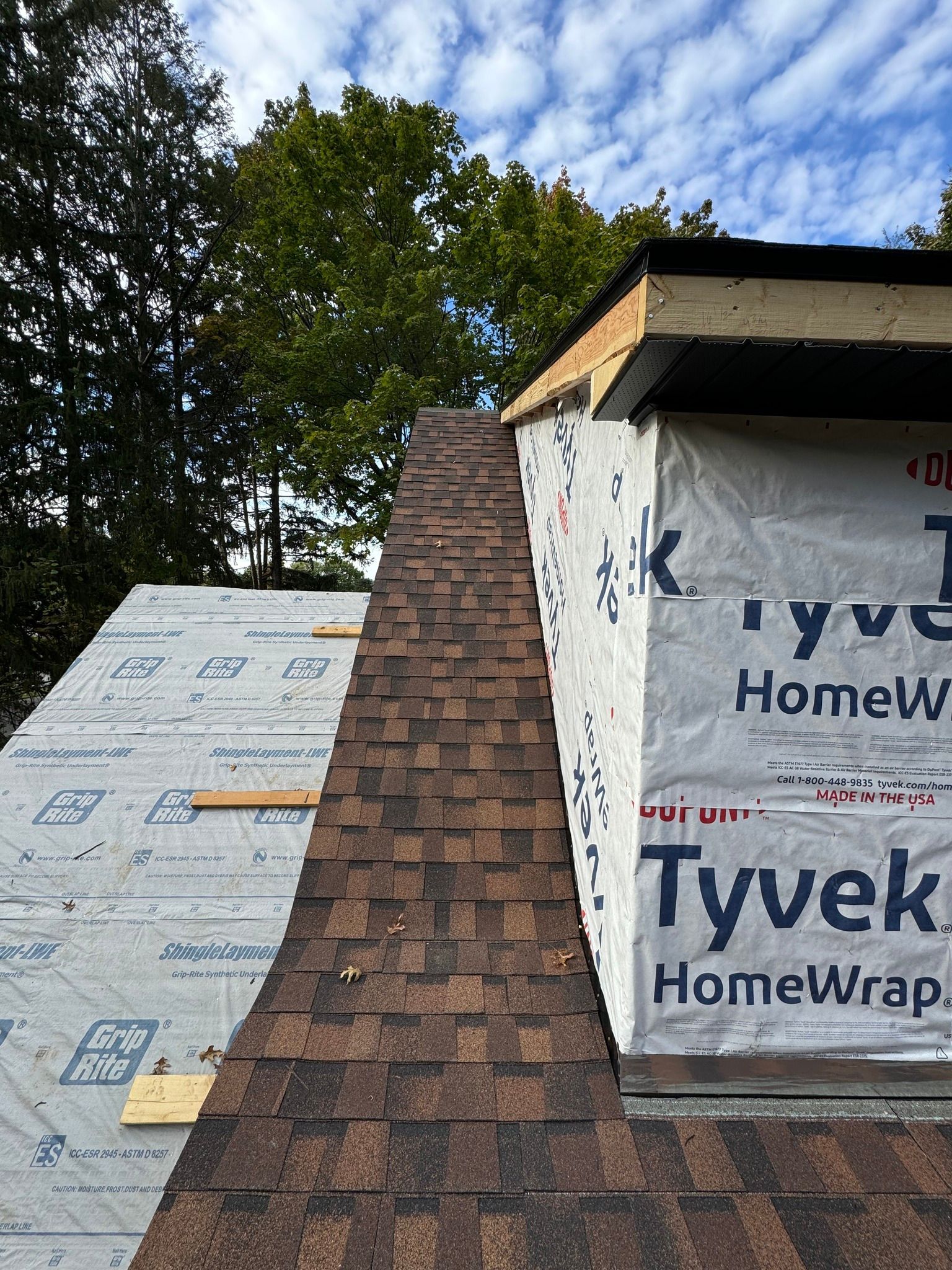 Roof in progress, brown shingles on one side, Tyvek HomeWrap on the other, cloudy sky.