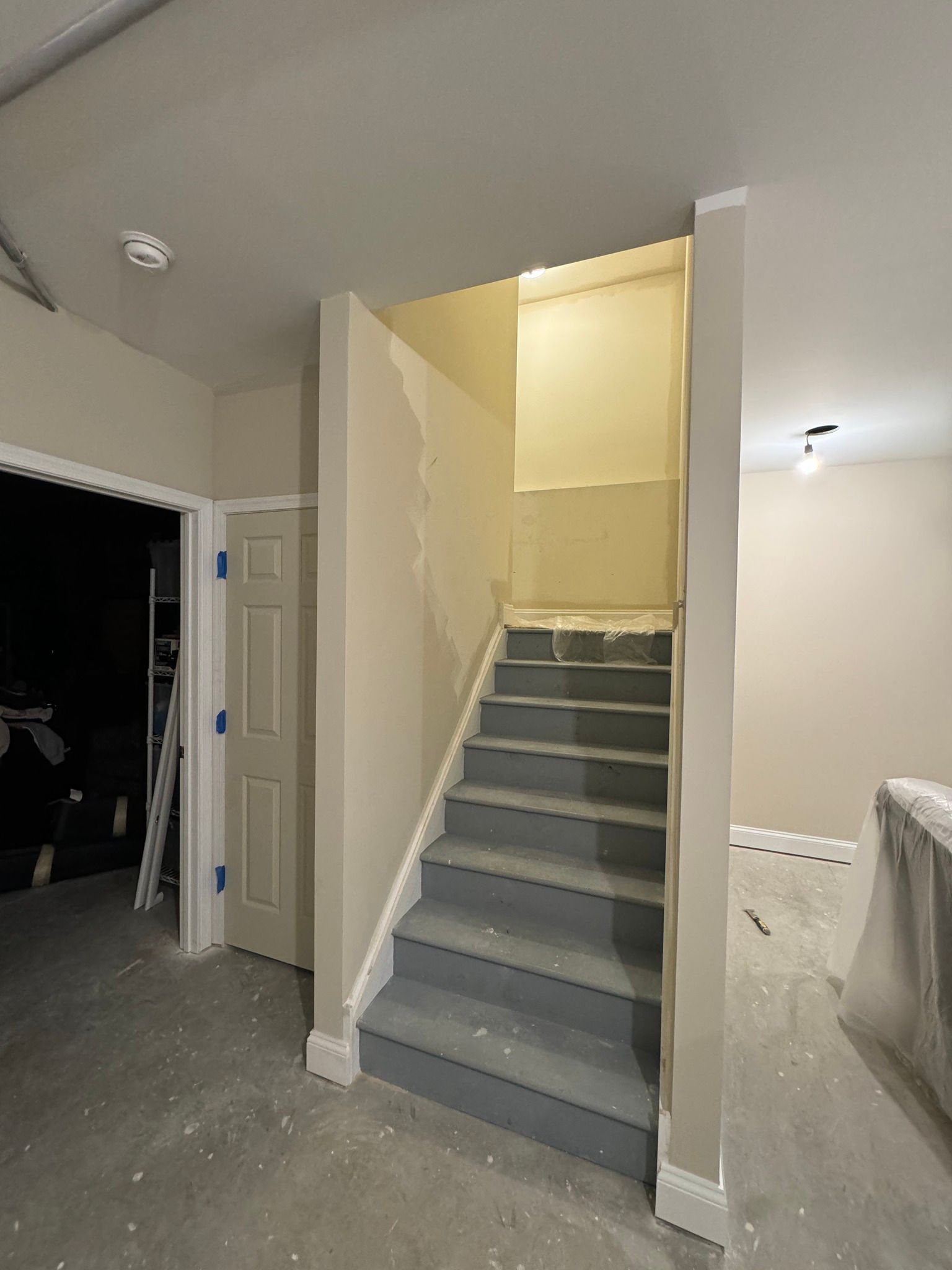 Staircase with gray carpet, leading up to a landing. Walls are neutral, in a room under construction.