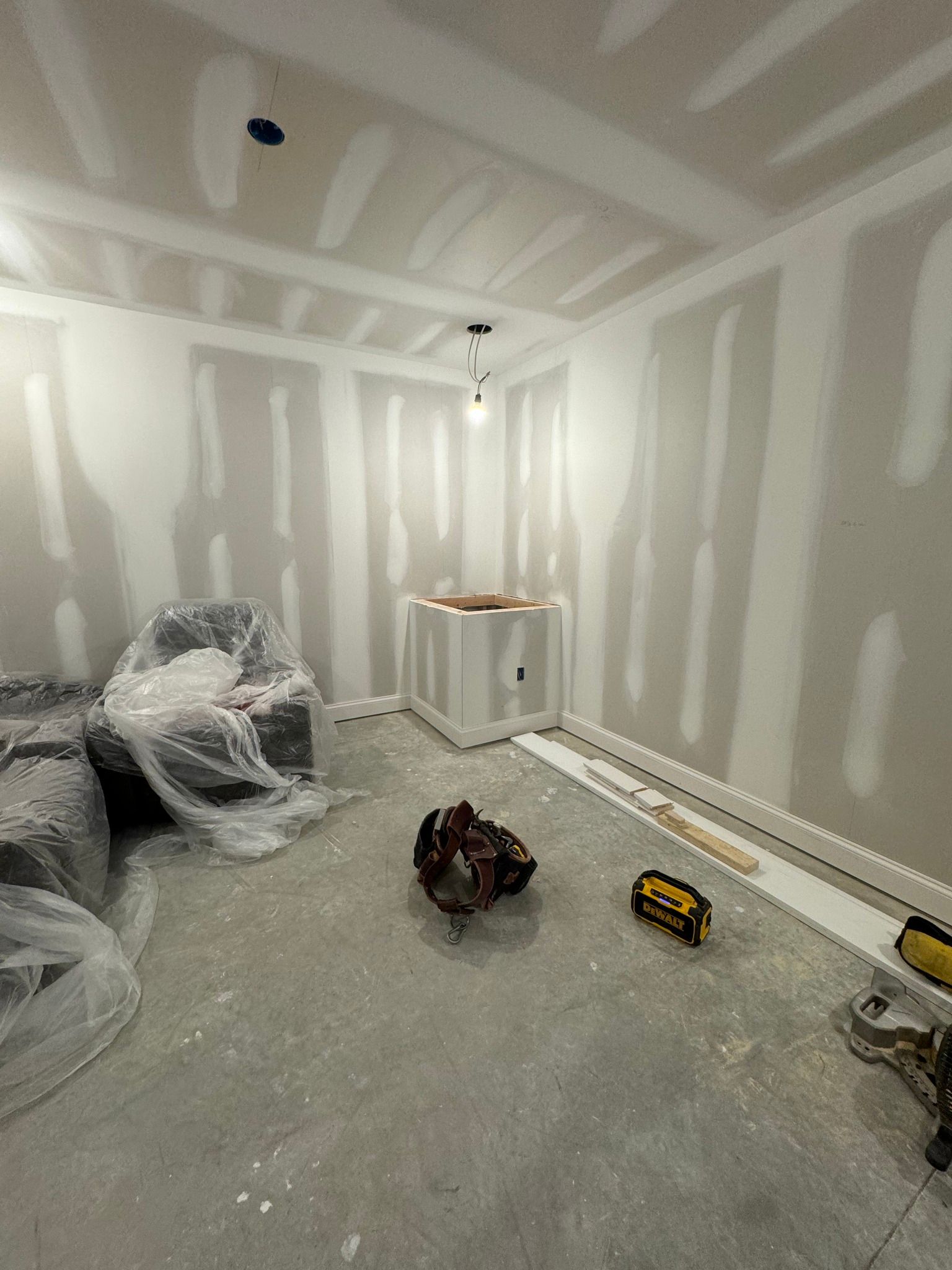 Interior room under construction, with drywall, unfinished ceiling, and construction materials.