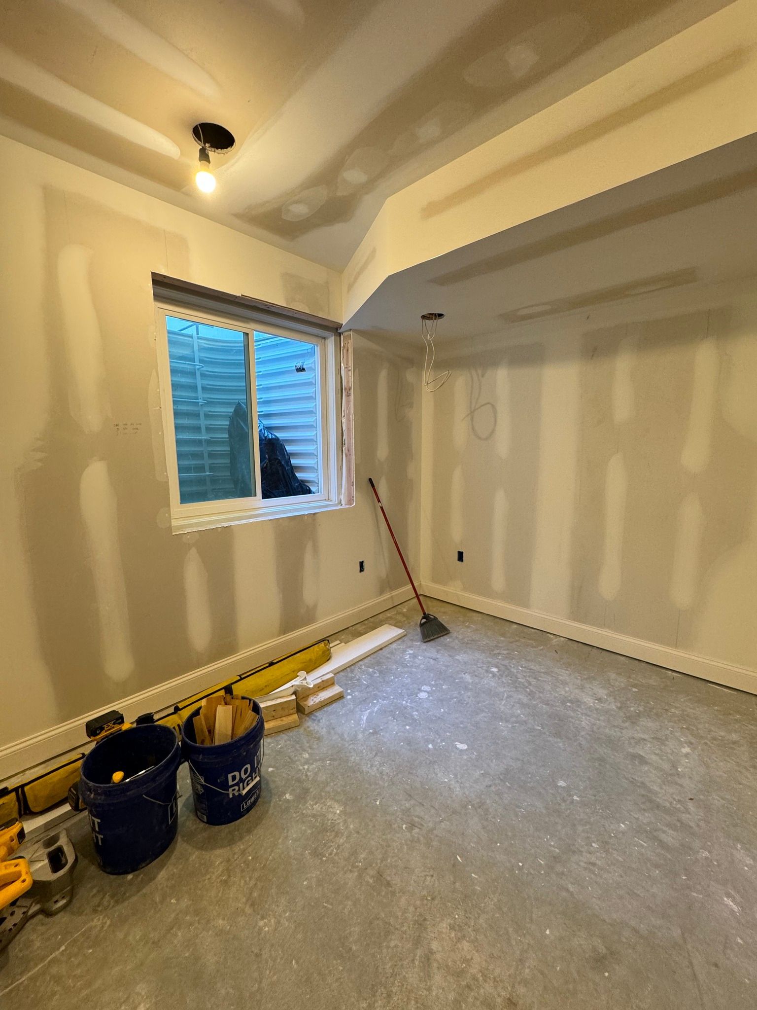 Room under construction, drywall installed. Window, tools, and buckets visible.