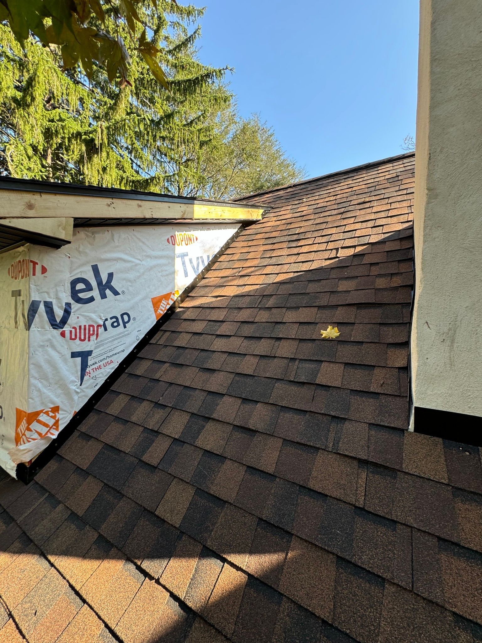 Roof with brown shingles, new construction visible. Tyvek wrap, wood framing, and a chimney.