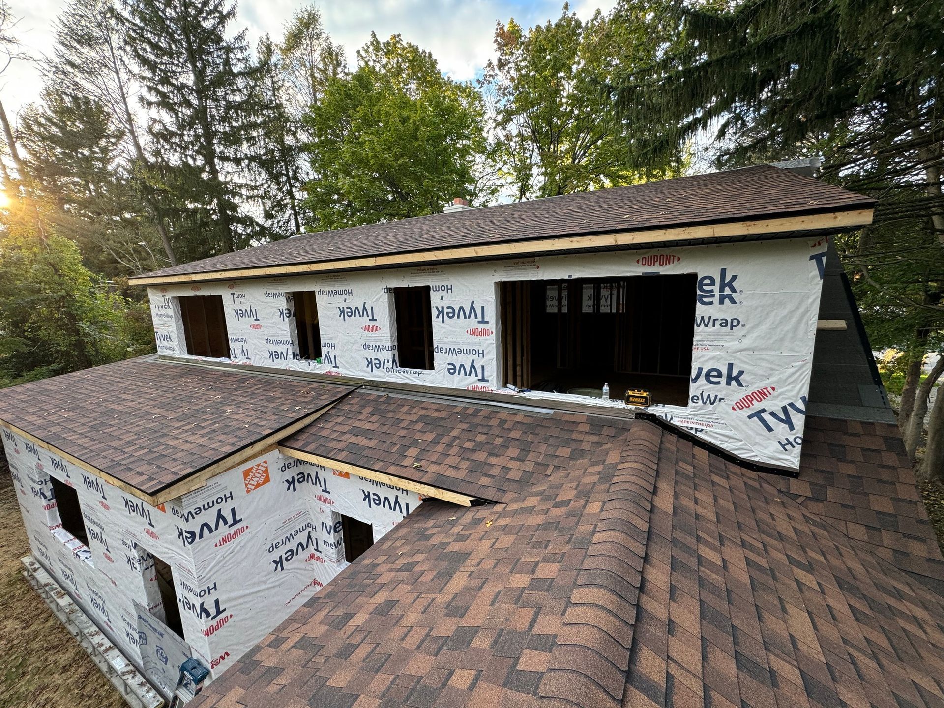 Construction of a house with brown shingles and a dormer. Building is wrapped in Tyvek.