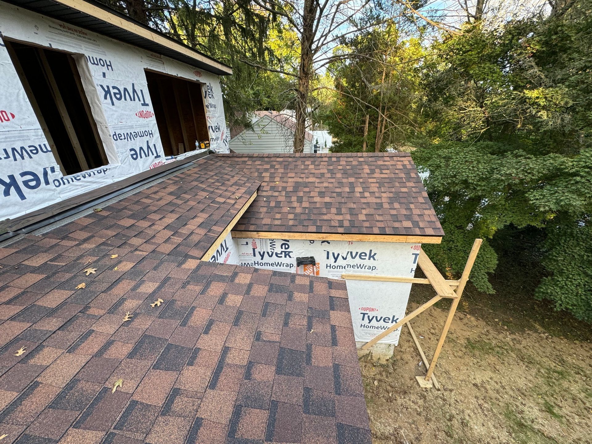 Roof construction in progress with brown shingles and Tyvek wrap.