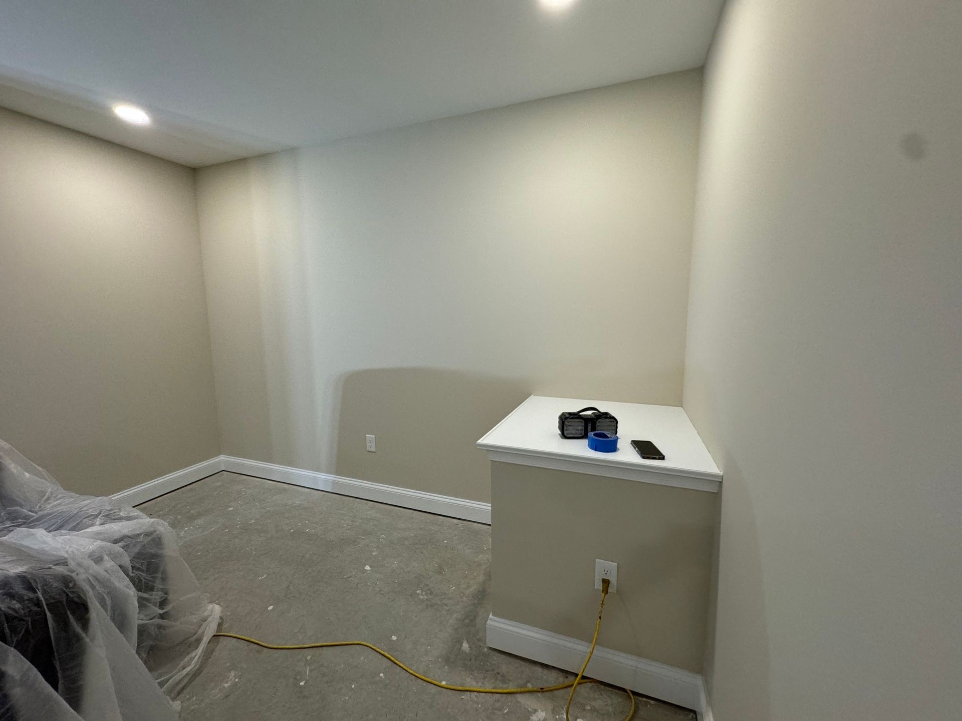 Empty room with off-white walls, a small table with items on it, and partially covered furniture.