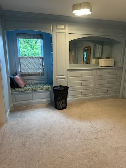 Bedroom with window seat, built-in drawers, and mirror framed by light blue cabinetry. Beige carpet.