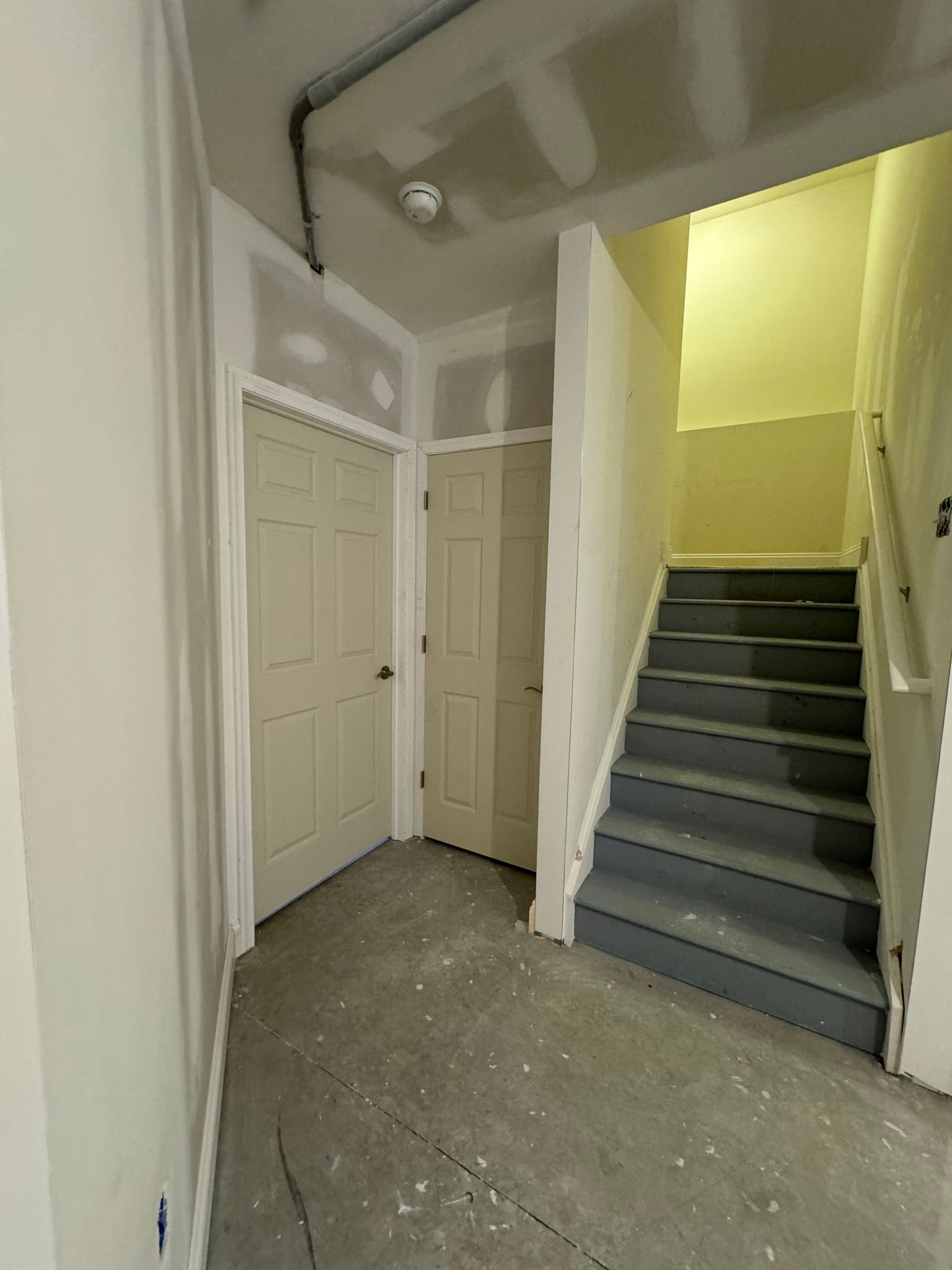 Hallway with unfinished walls, doors, and stairs leading up.