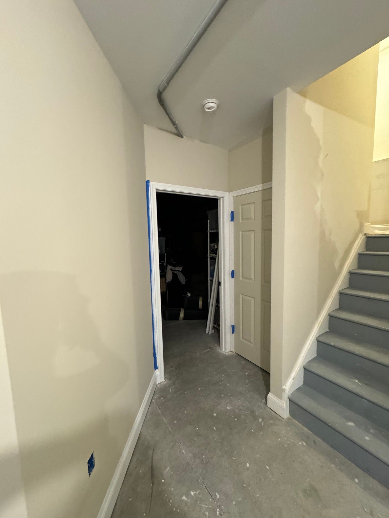A hallway with a door, stairs, and a visible electrical cable. Walls are painted light beige.