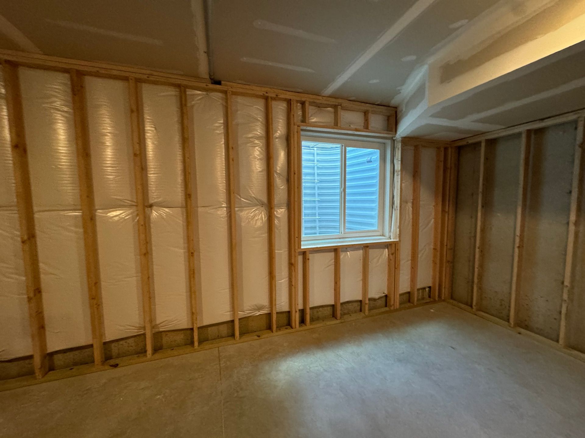 Interior framing of a room with insulation and a window. Walls are unfinished with bare wood studs.
