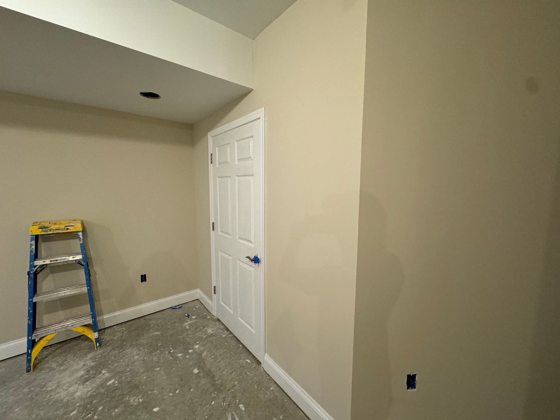 A room with beige walls, a white door, and a blue and yellow ladder.