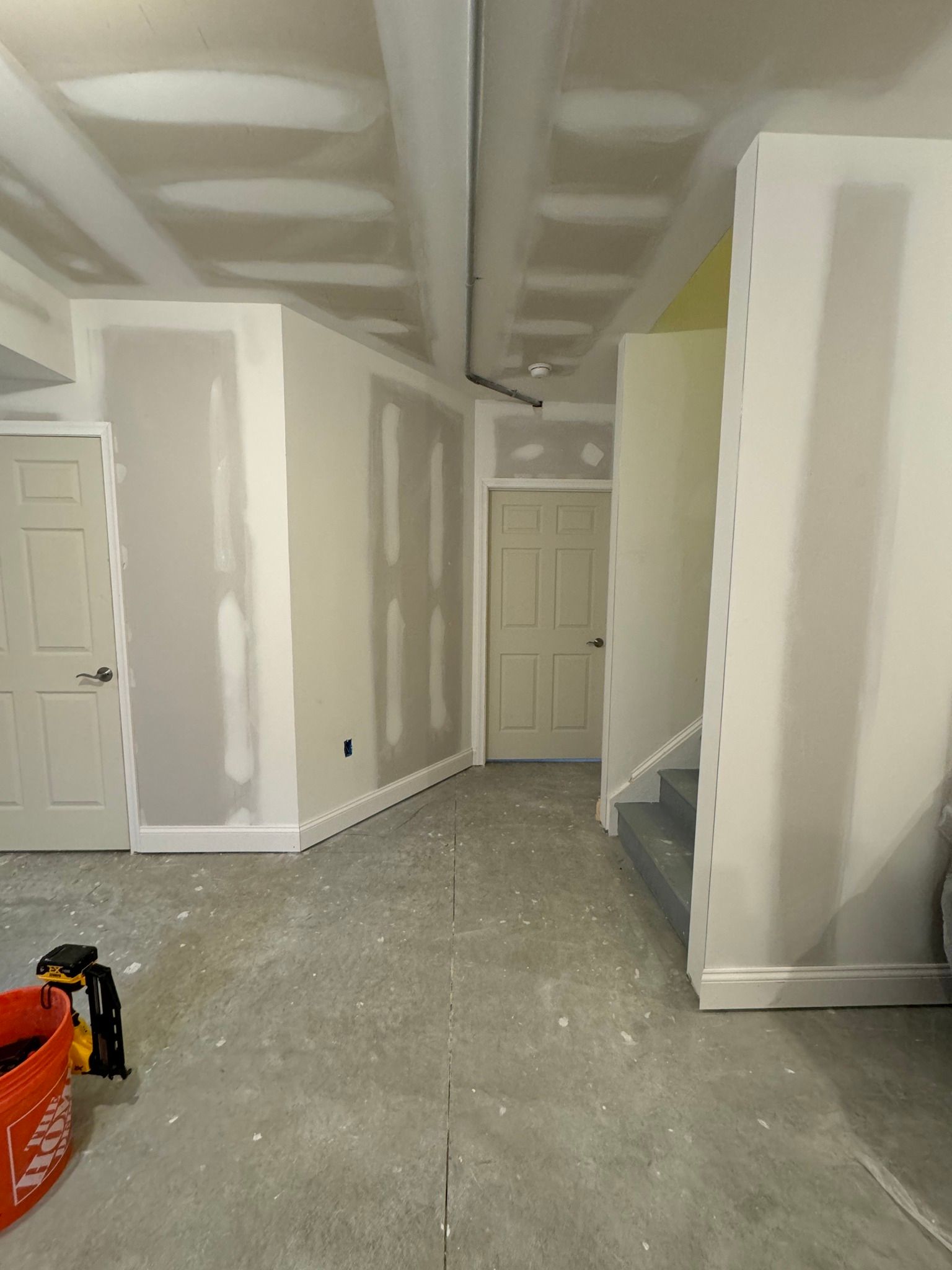 Interior of a room under construction, with drywall, unfinished ceiling, and a doorway.