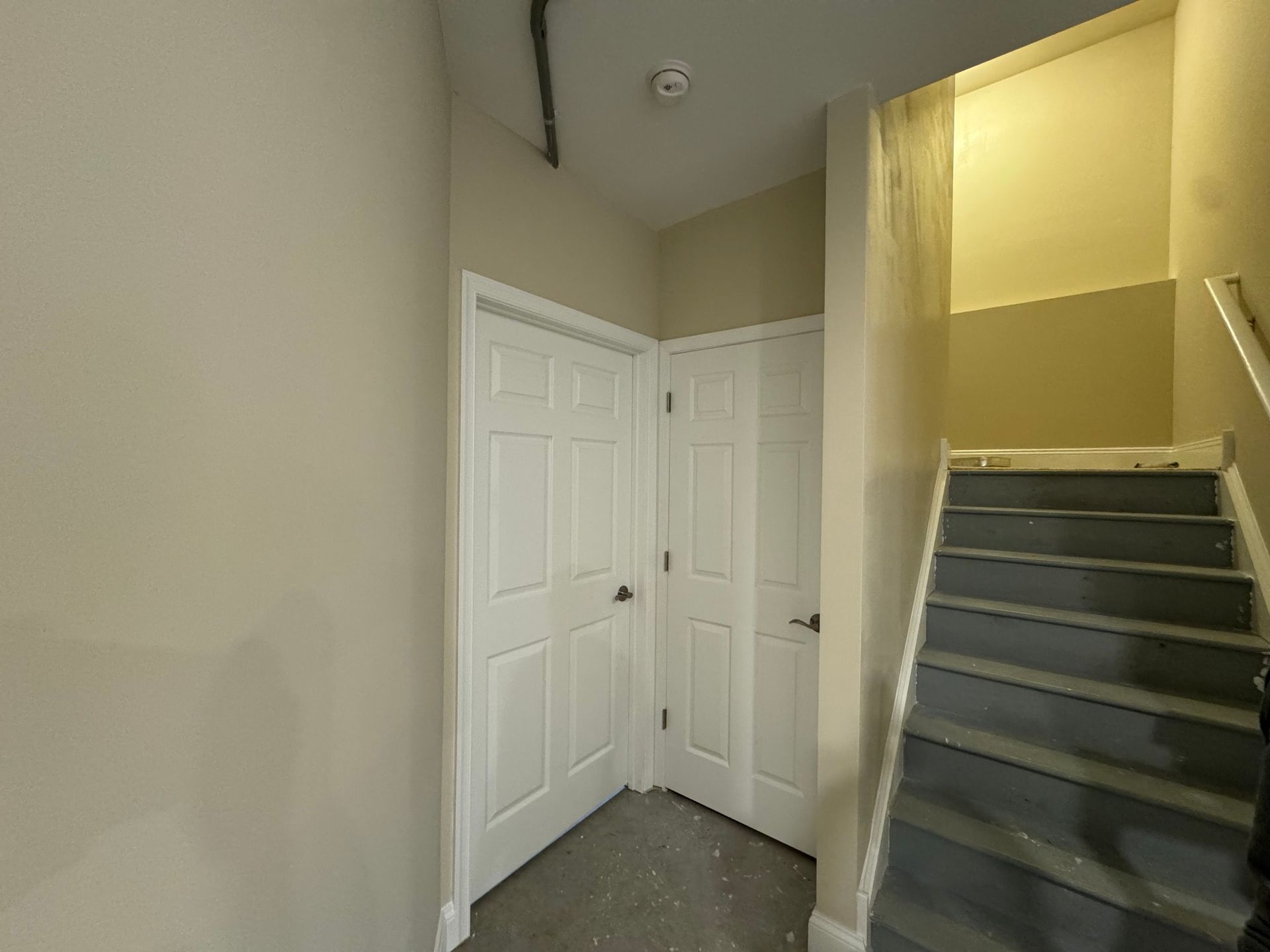 Entryway with two white doors, gray stairs, and beige walls.