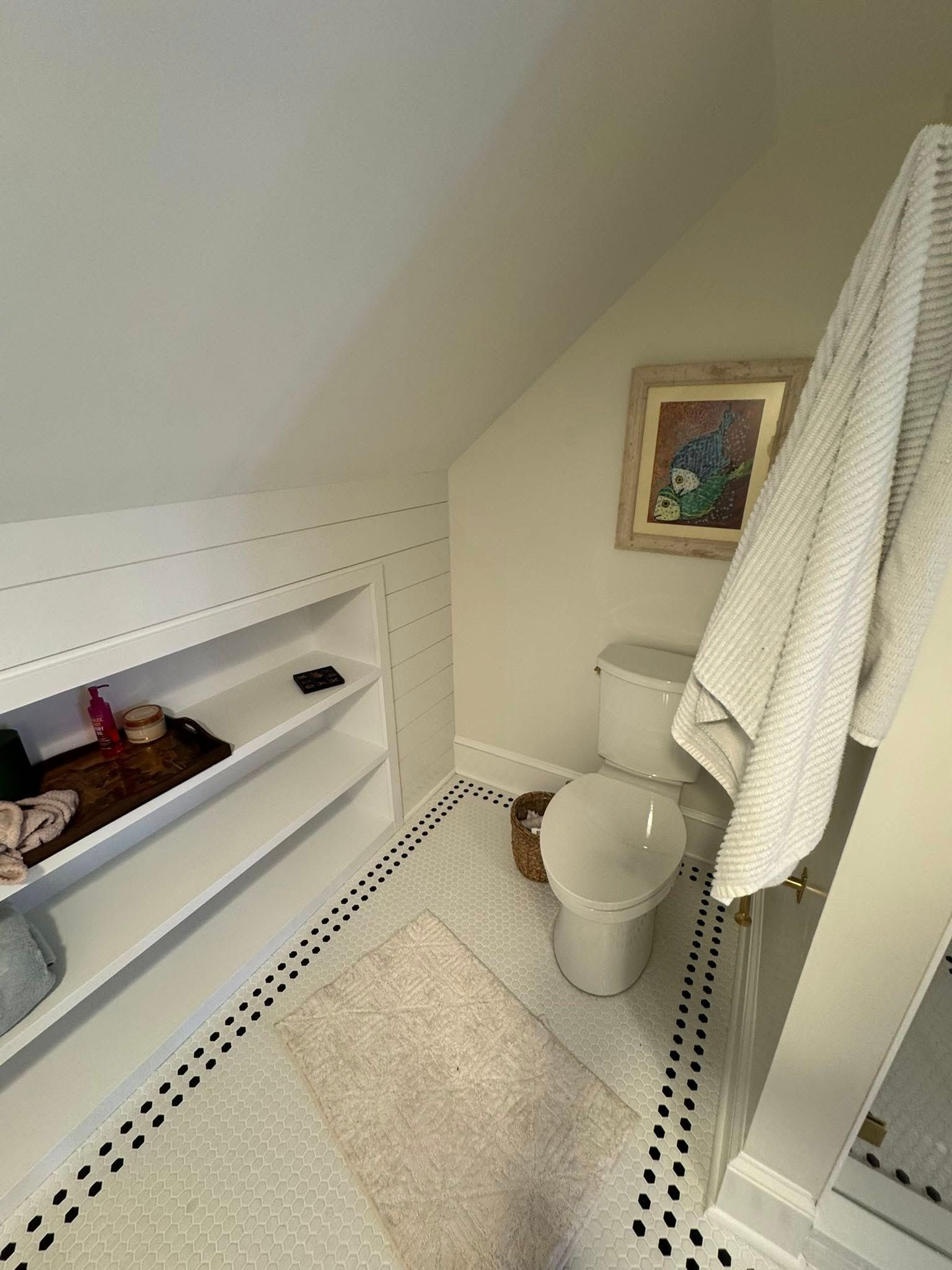 Bathroom with a toilet, towel, shelves, and a patterned floor.