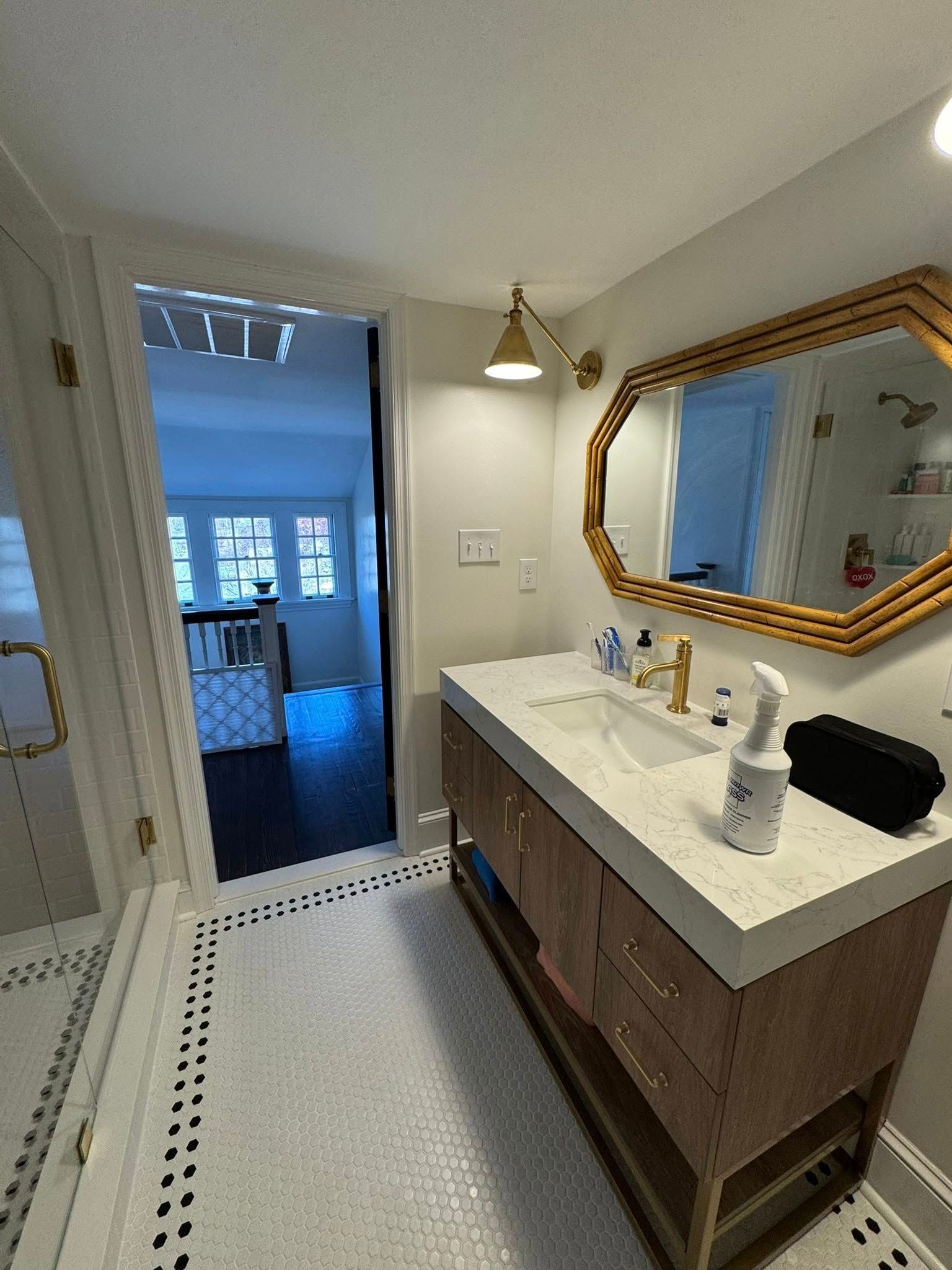 Bathroom with vanity, mirror, and doorway to another room. Gold accents. White and black tile floor.