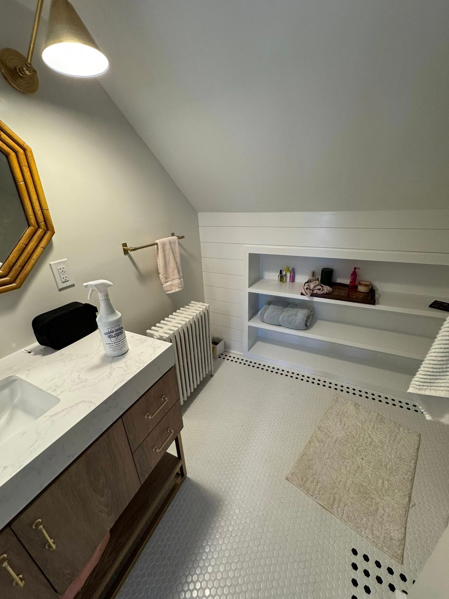 Bathroom with angled ceiling, vanity, gold mirror, shelving unit, and mosaic tile floor.