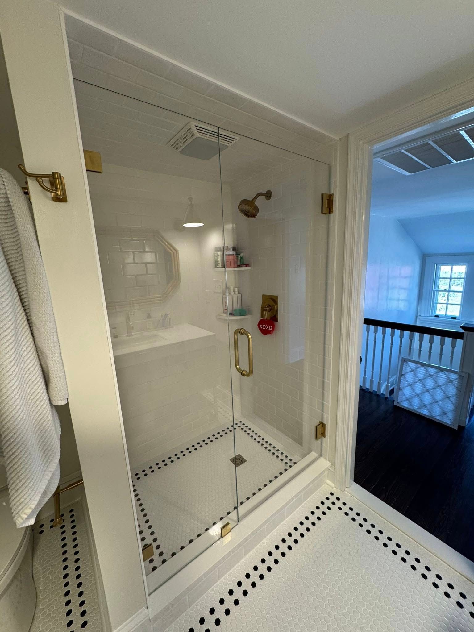 Bathroom with glass shower, white and black tile, gold fixtures, and an open doorway to a hallway.
