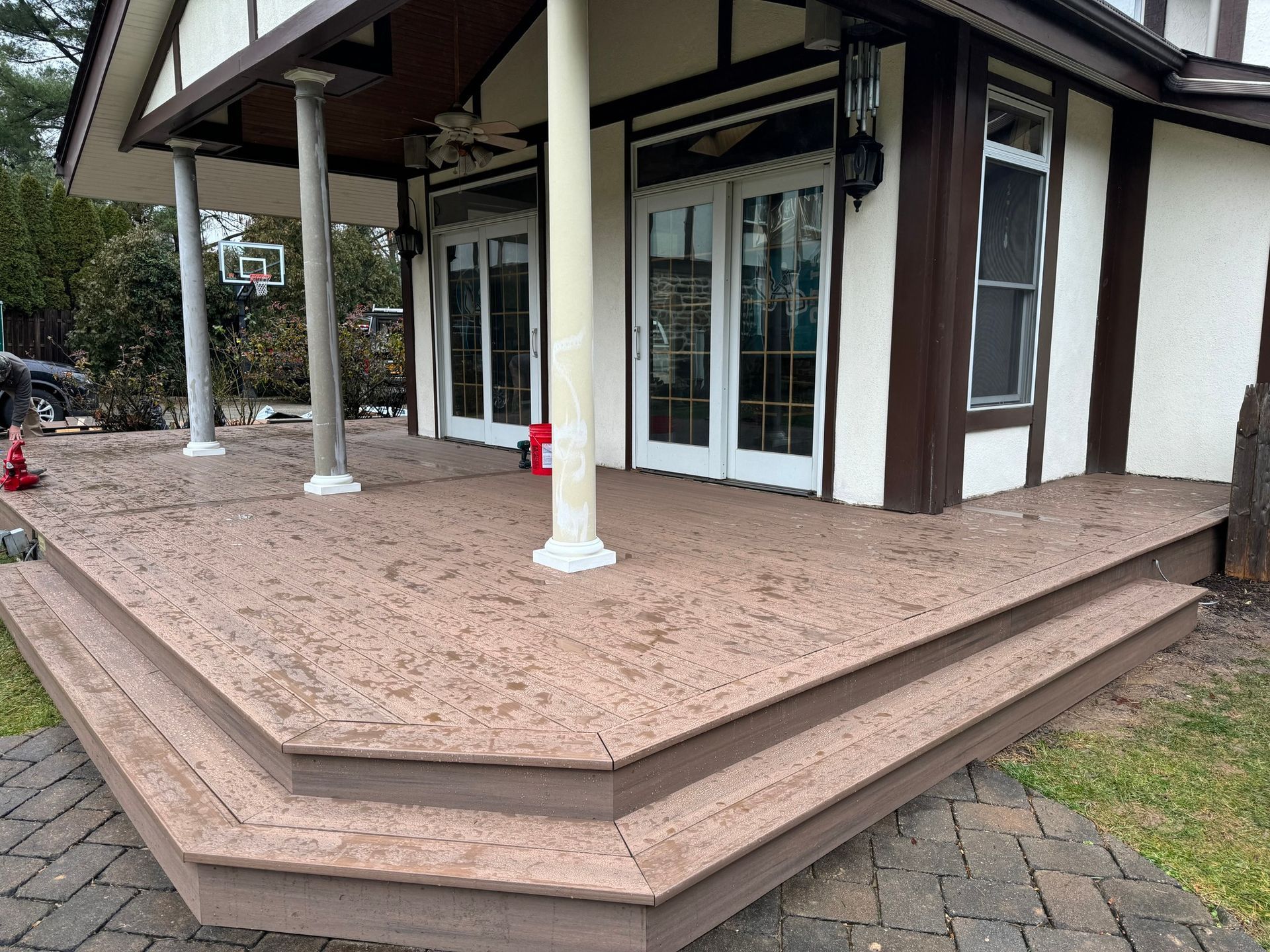 Brown composite deck with steps in front of a house. White columns support the porch roof.