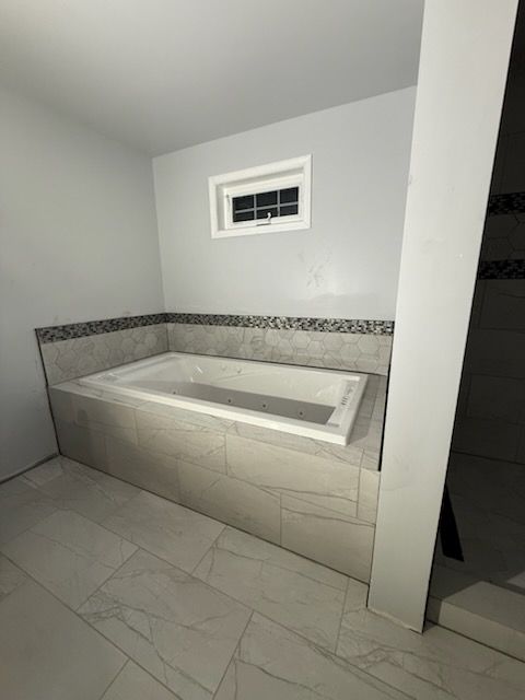 Bathroom with a built-in rectangular bathtub, tiled walls and floor, and a small window.