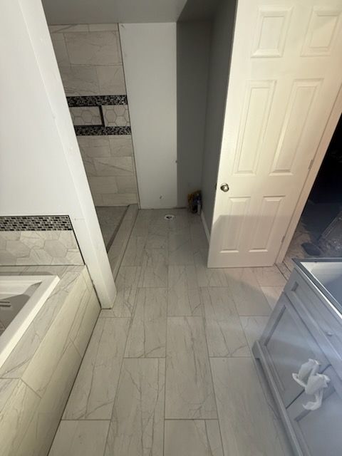 Bathroom with tiled floor and shower, door, and vanity. Mostly white and gray.