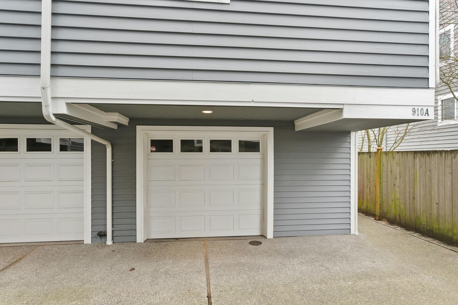 Garage doors under a gray building, with concrete ground and wooden fence.