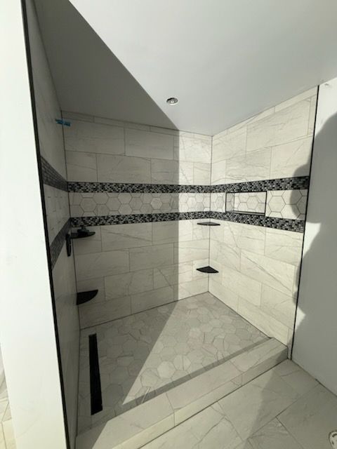 Finished shower stall with white and gray tile, black accents, and built-in shelves.
